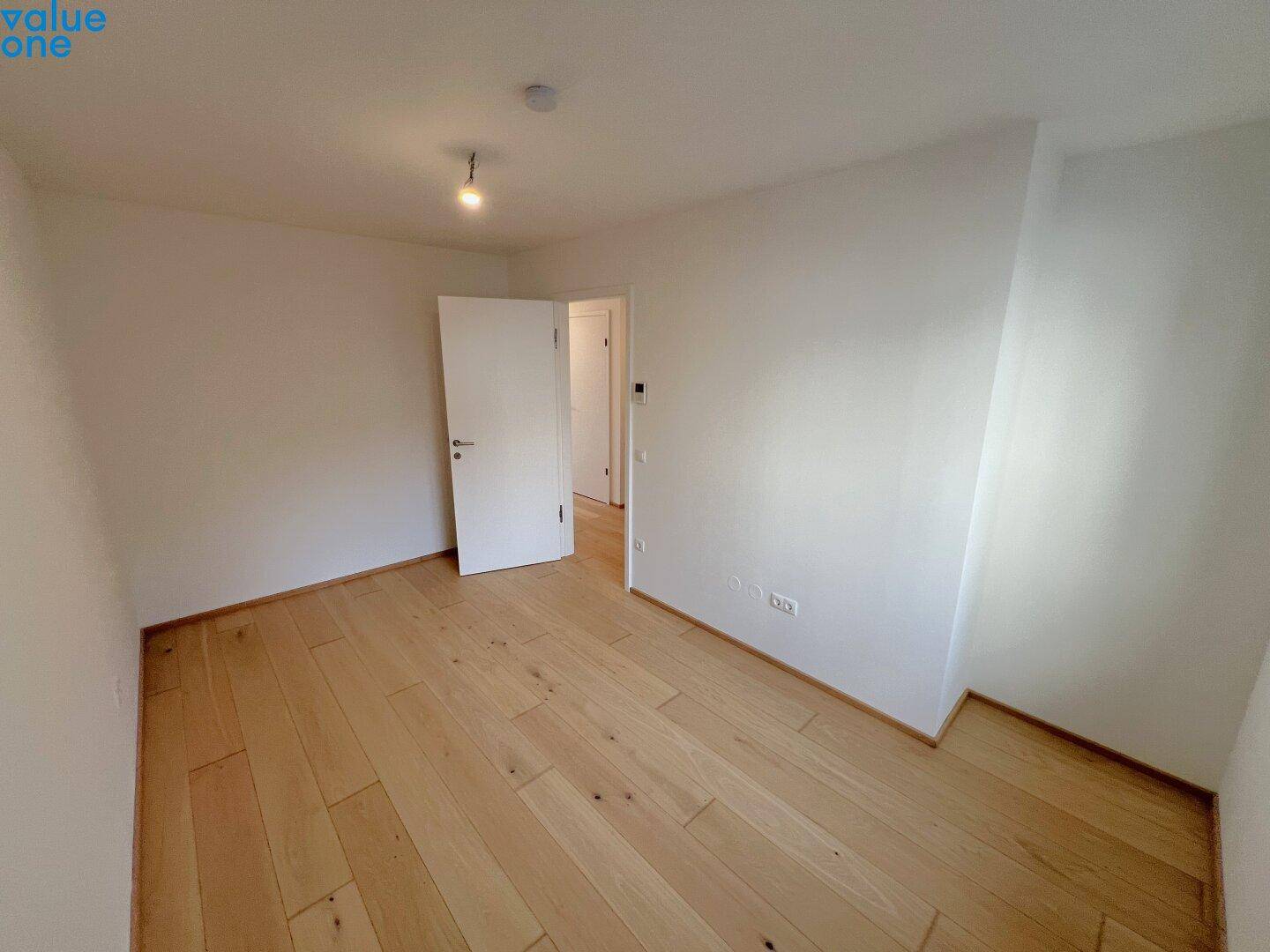 Leeres Zimmer mit hellem Holzboden und weißen Wänden, bereit zur individuellen Gestaltung.