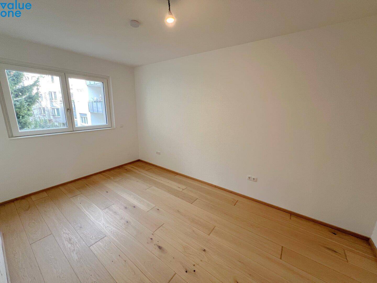 Helles Zimmer mit Holzboden und Fenster, das viel Tageslicht hereinlässt.