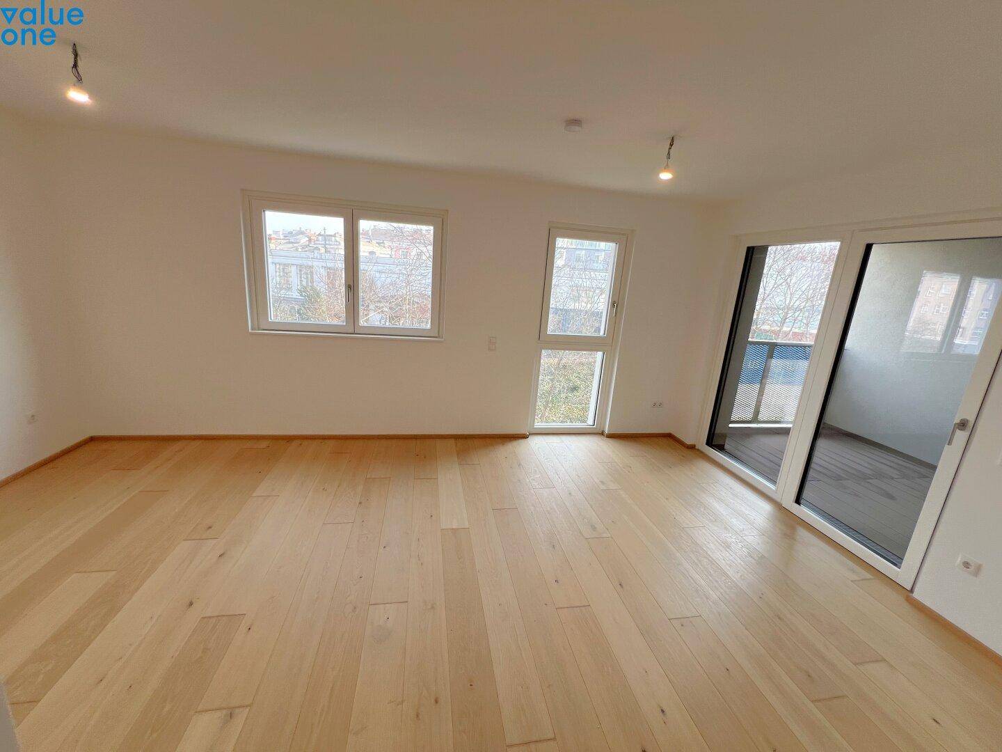 Geräumiger Wohnbereich mit Holzboden, großen Fenstern und direktem Zugang zum Balkon.