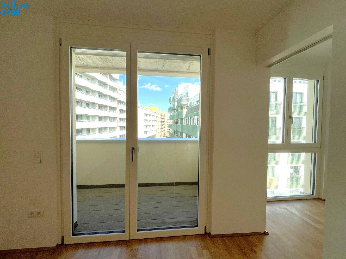 Blick vom Wohnzimmer auf den leeren Balkon mit Holzboden und Stadtblick.