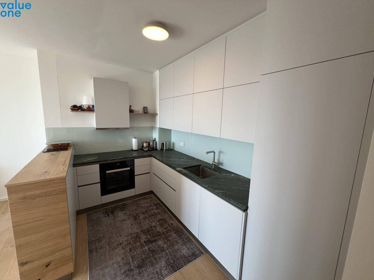 Moderne Küche mit weißen Schränken, dunkler Arbeitsplatte und Holzelementen, gut beleuchtet.