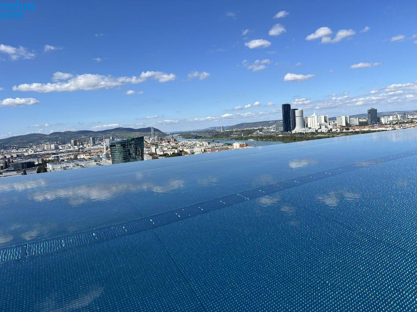 Dachpool mit weitem Blick über die Stadt, den Fluss und moderne Hochhäuser unter blauem Himmel.