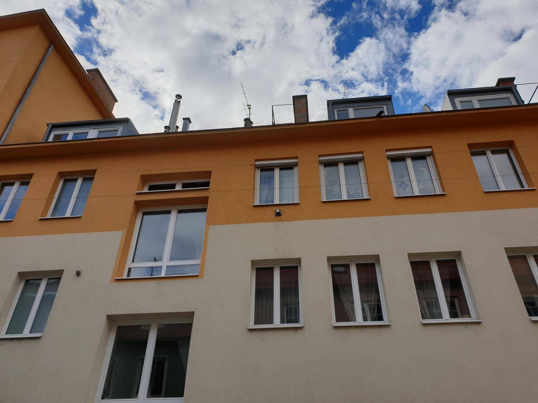 Fassade eines Mehrfamilienhauses mit orangefarbenen und beigefarbenen Akzenten unter blauem Himmel.