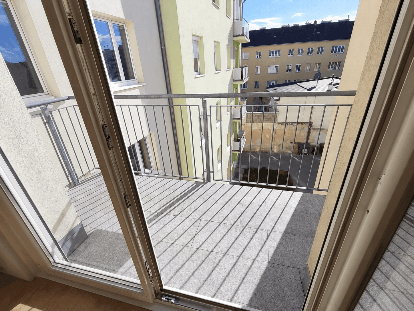 Geräumiger Balkon mit Fliesenboden und Metallgeländer, bietet einen Blick auf den Innenhof.