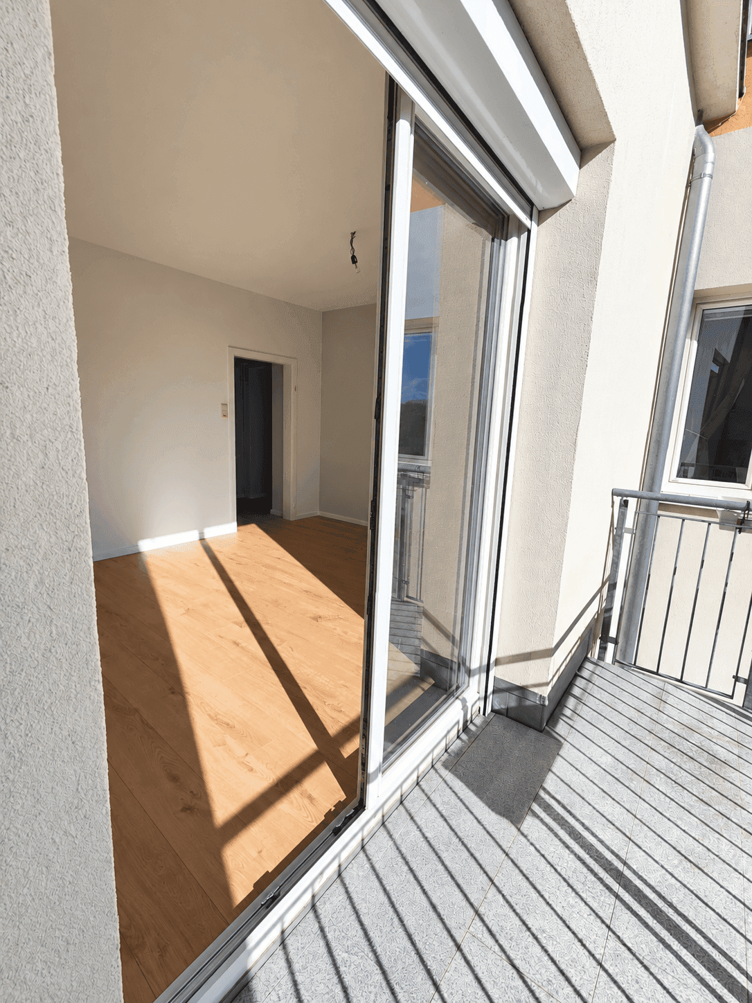 Heller Balkon mit Fliesenboden und Blick auf die Umgebung, zugänglich durch eine große Schiebetür.