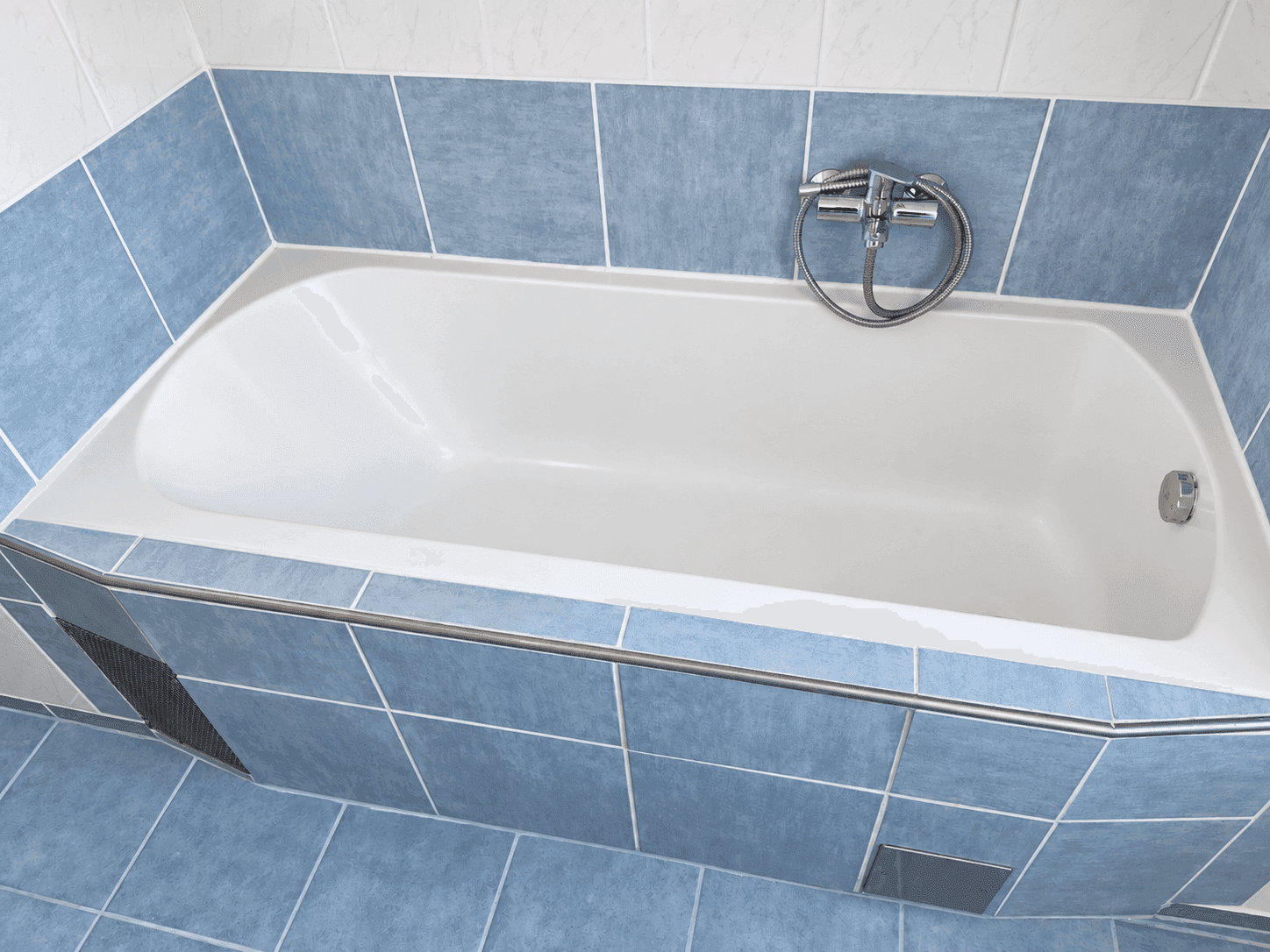 Nahaufnahme einer Badewanne mit blauen und weißen Fliesen, sauber und funktionsbereit.