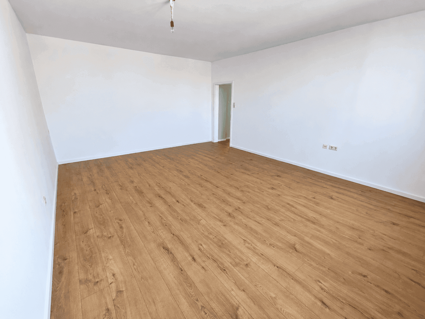 Geräumiges, leeres Zimmer mit hellem Laminatboden und weißen Wänden, bereit zur individuellen Gestaltung.