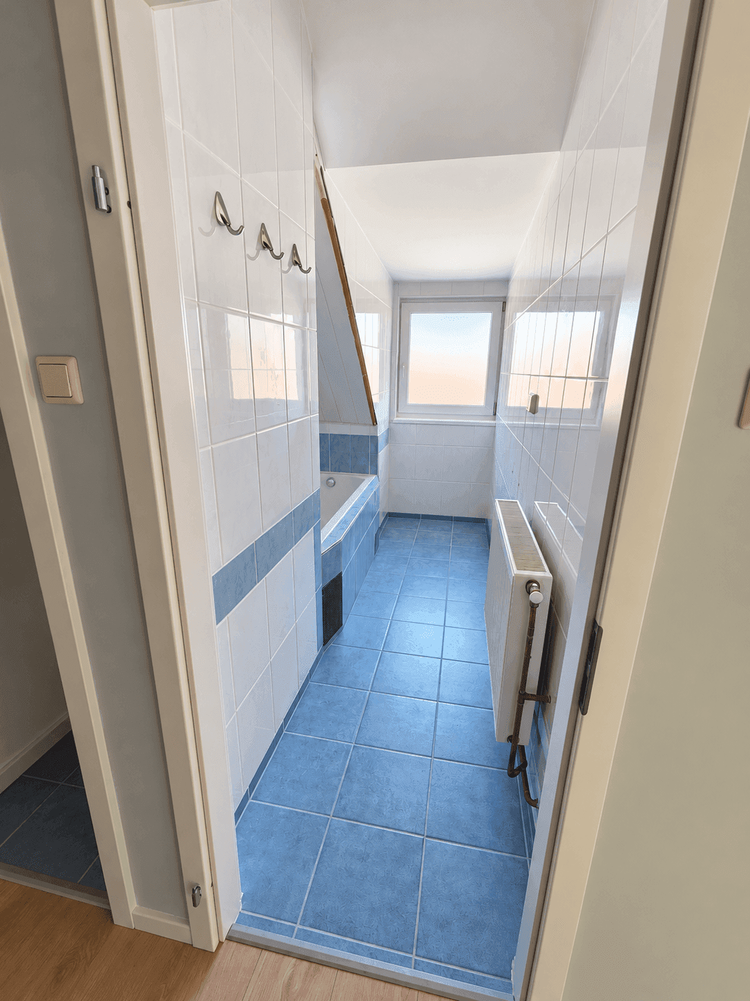 Badezimmer mit blauen und weißen Fliesen, Badewanne und Fenster, das Tageslicht hereinlässt.