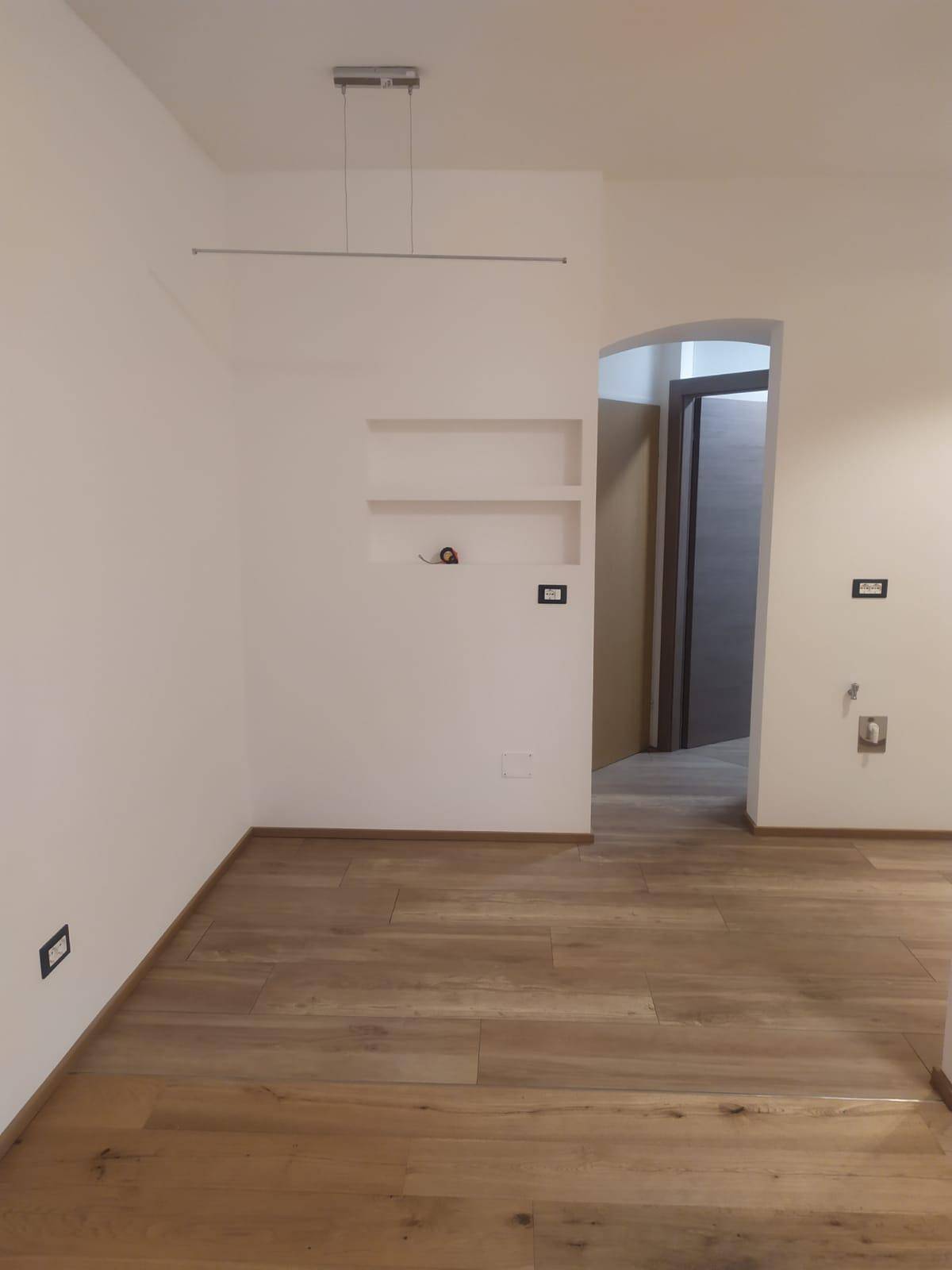 Leerer Wohnbereich mit Holzoptik-Fliesenboden und eingebauten Wandnischen, bereit zur Gestaltung.