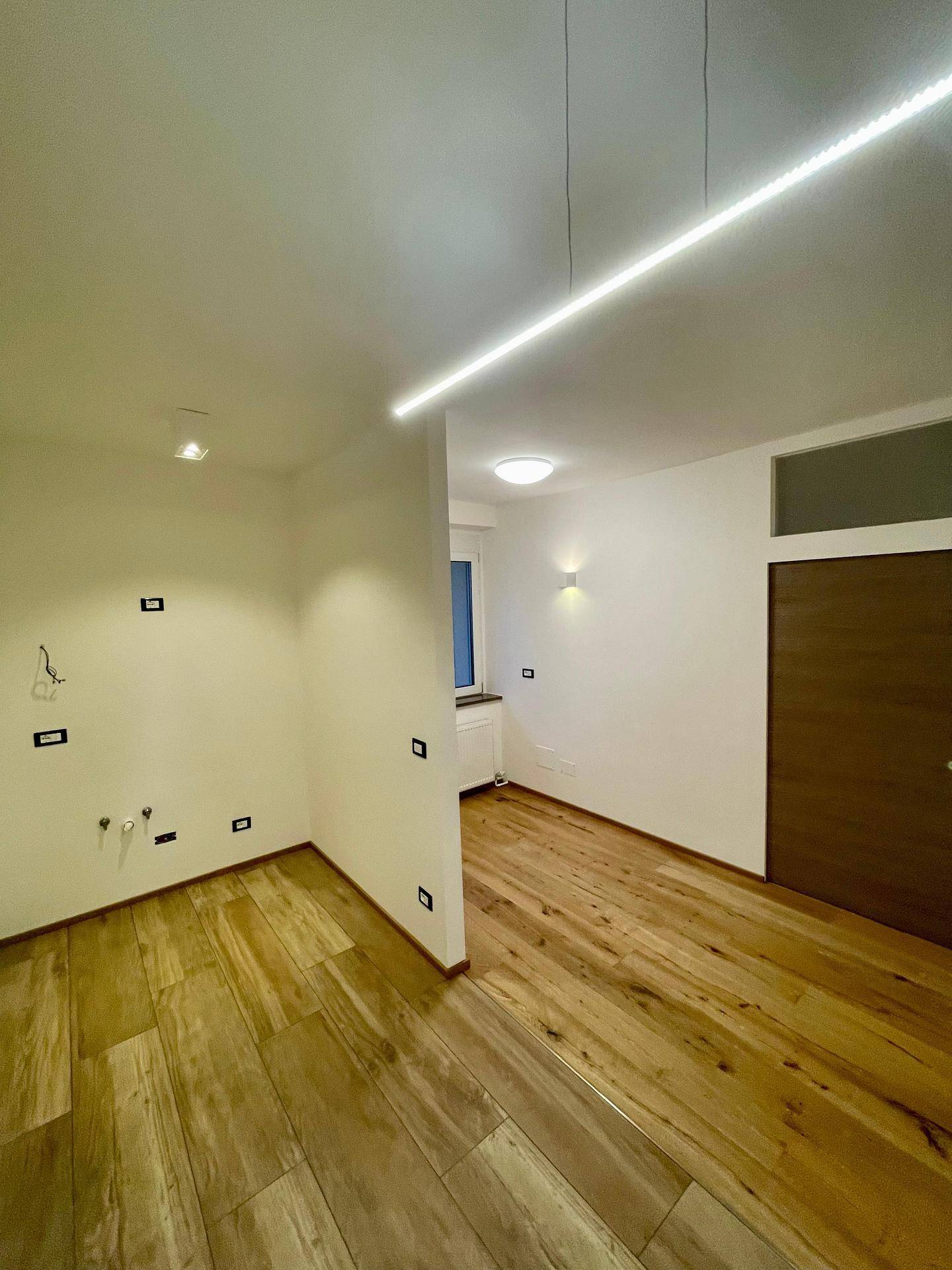 Heller Küchenbereich mit Holzoptik-Fliesenboden und modernen Lichtelementen, bereit für die Einrichtung.