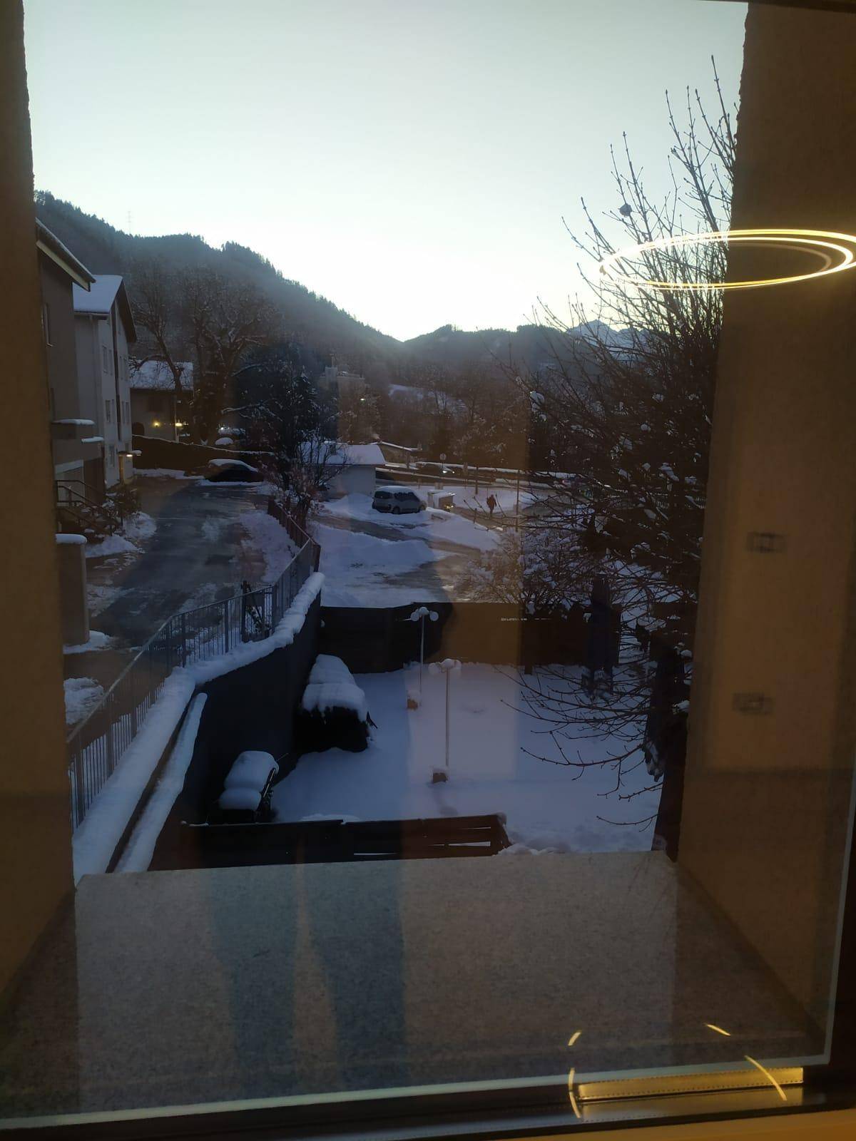 Winterlicher Ausblick aus dem Fenster auf einen verschneiten Innenhof und umliegende Berge.
