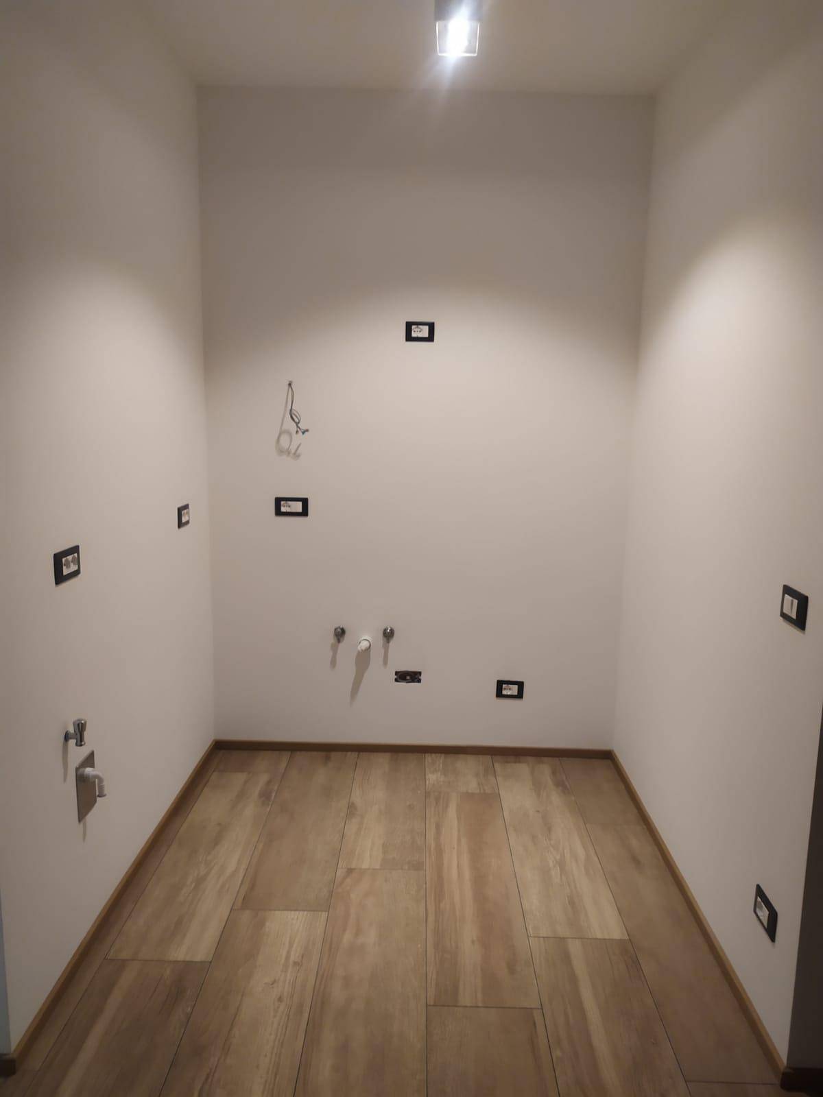 Kleiner Raum mit Holzoptik-Fliesenboden und Wasseranschlüssen, ideal als Waschküche.