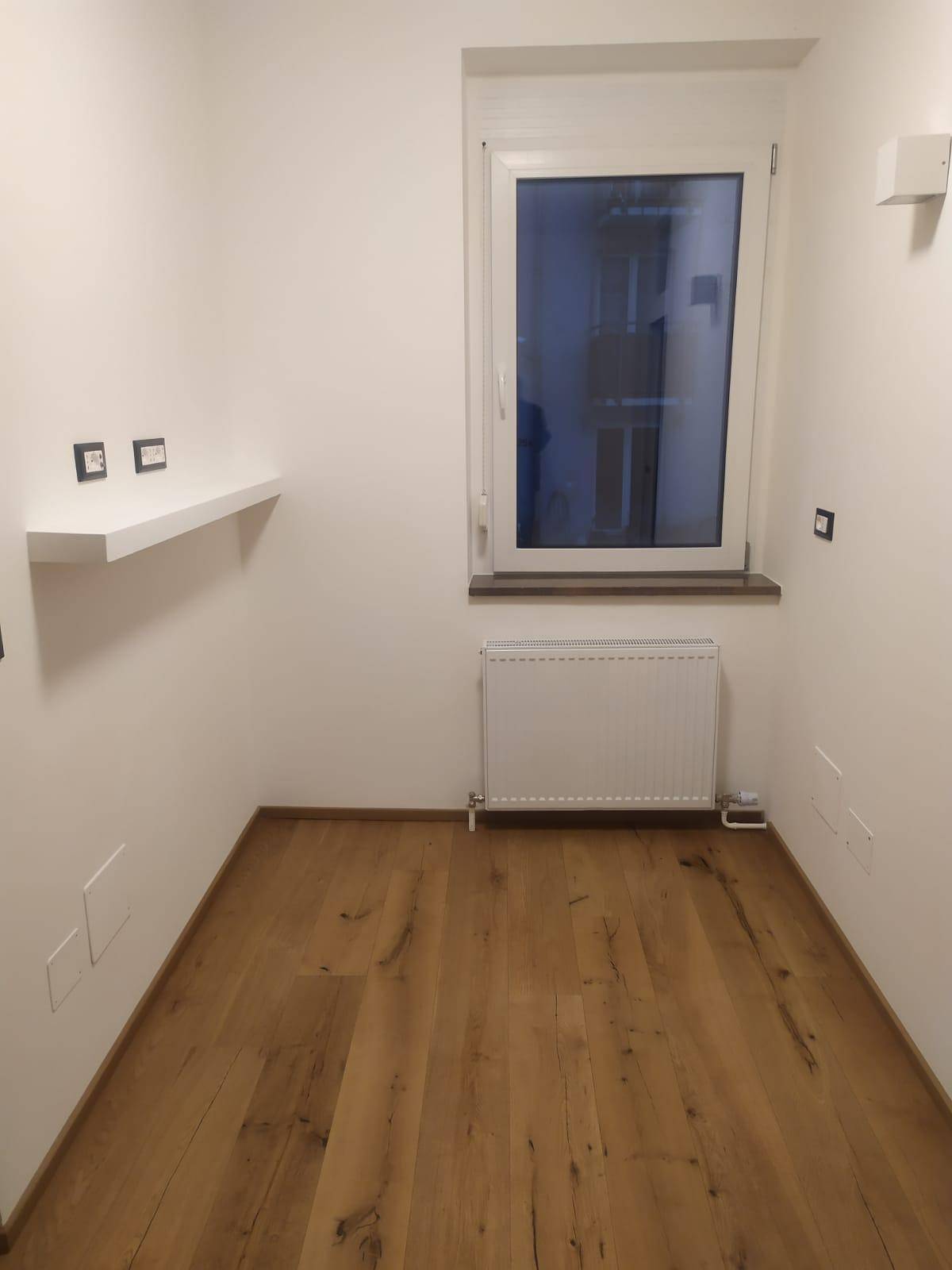 Kleiner, heller Raum mit Holzoptik-Fliesenboden, Fenster und Heizkörper, ideal als Abstellraum.