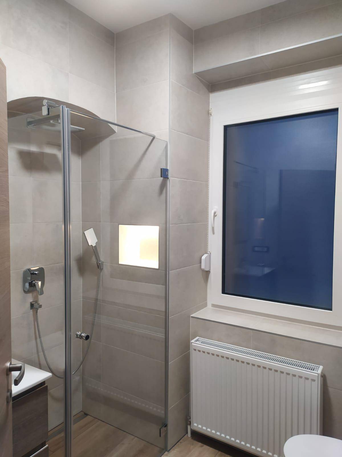 Modernes Badezimmer mit begehbarer Dusche, hellen Fliesen und Fenster für Tageslicht.