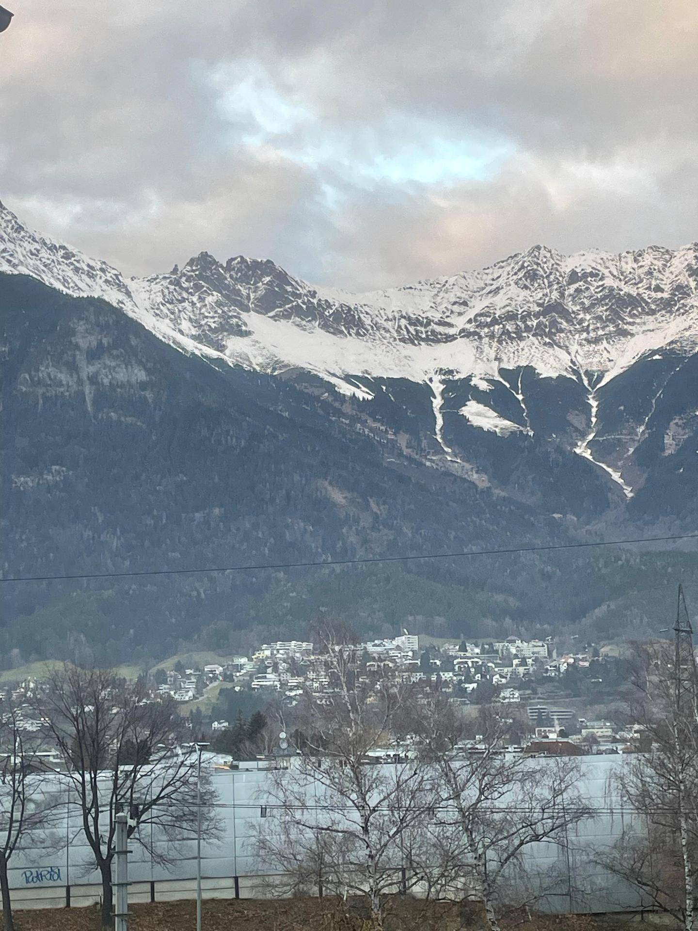 Panoramablick auf schneebedeckte Berge und eine darunterliegende Siedlung.