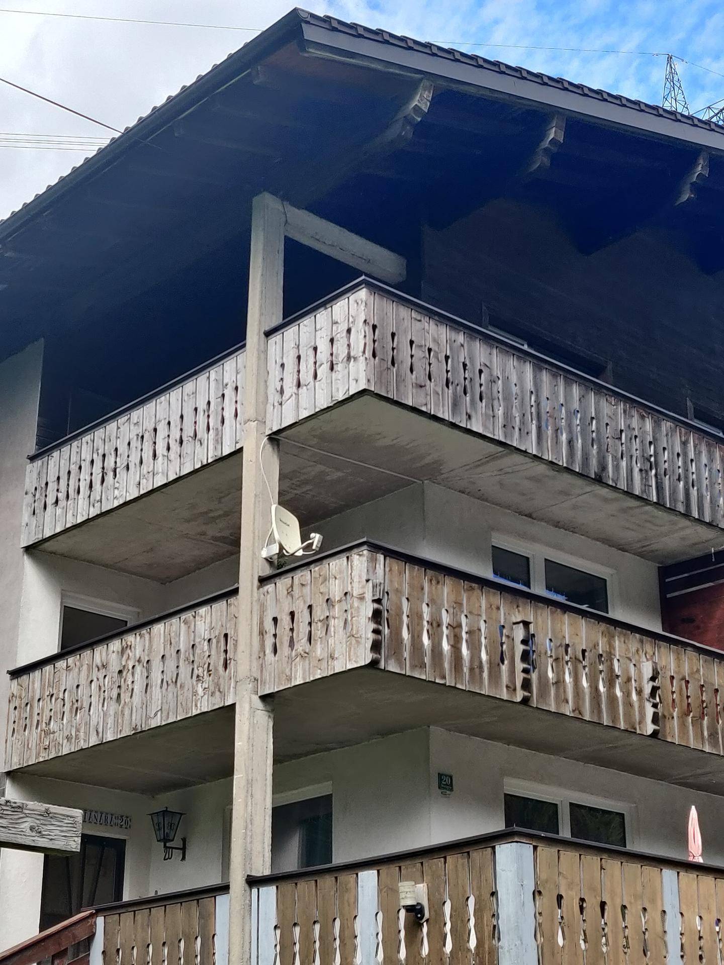 Fassade eines Gebäudes mit mehreren Balkonen und Holzgeländern in alpiner Umgebung.