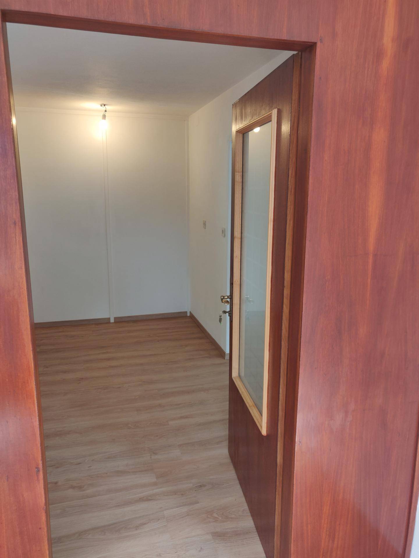 Leerer Raum mit hellem Laminatboden, gesehen durch eine Holztüröffnung.
