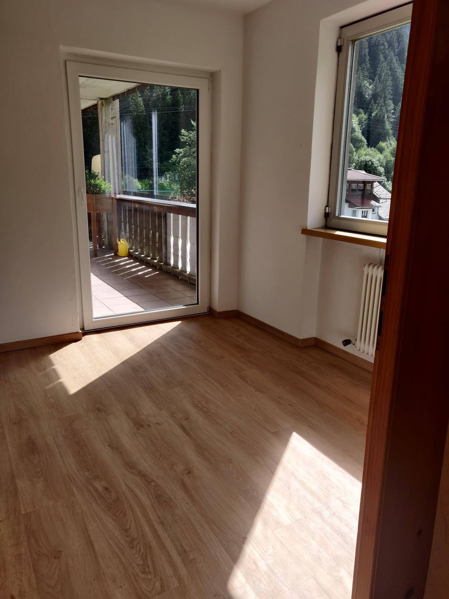 Heller Raum mit Laminatboden, Fenster und Zugang zu einem Balkon mit Bergblick.
