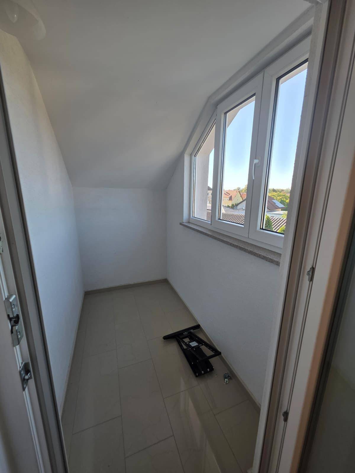 Kleine, helle Loggia mit Fliesenboden und Fenstern, die einen Blick nach draußen bieten.