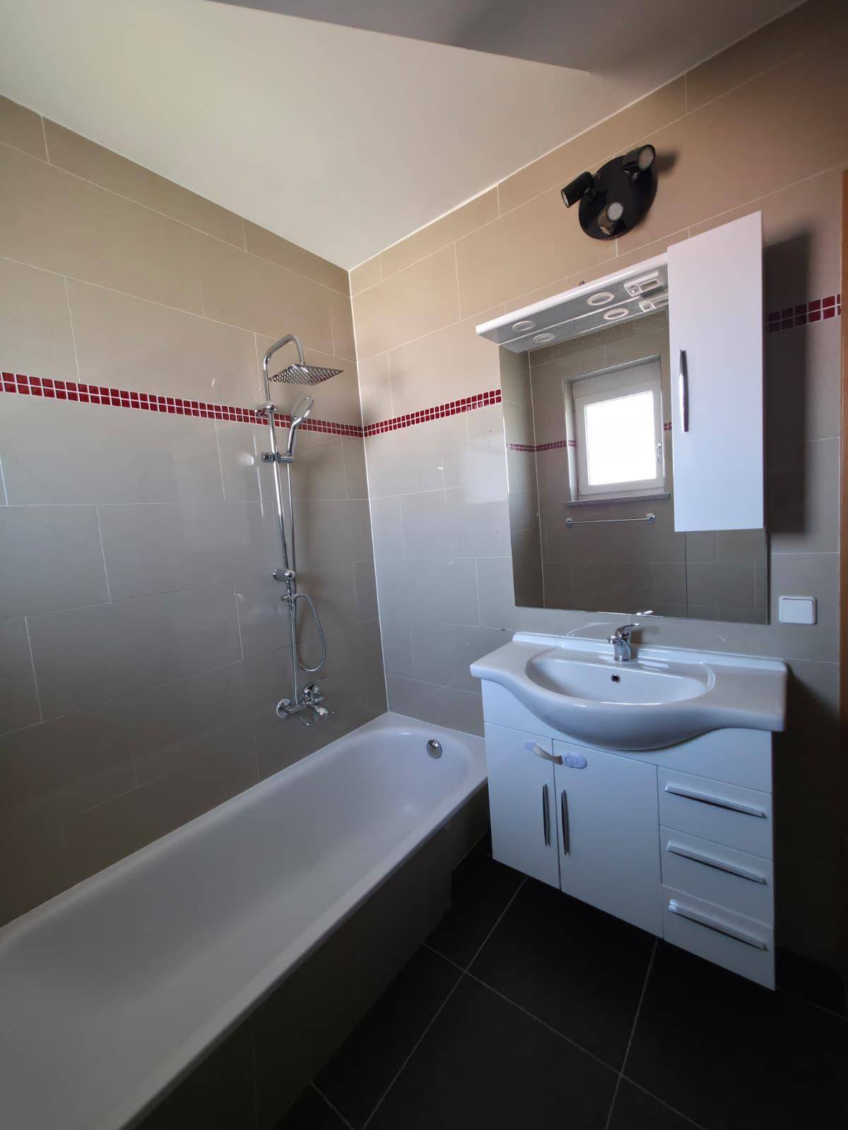 Funktionales Badezimmer mit Badewanne, Duscharmatur, Waschtisch und Spiegelschrank, mit Fenster im Spiegel.