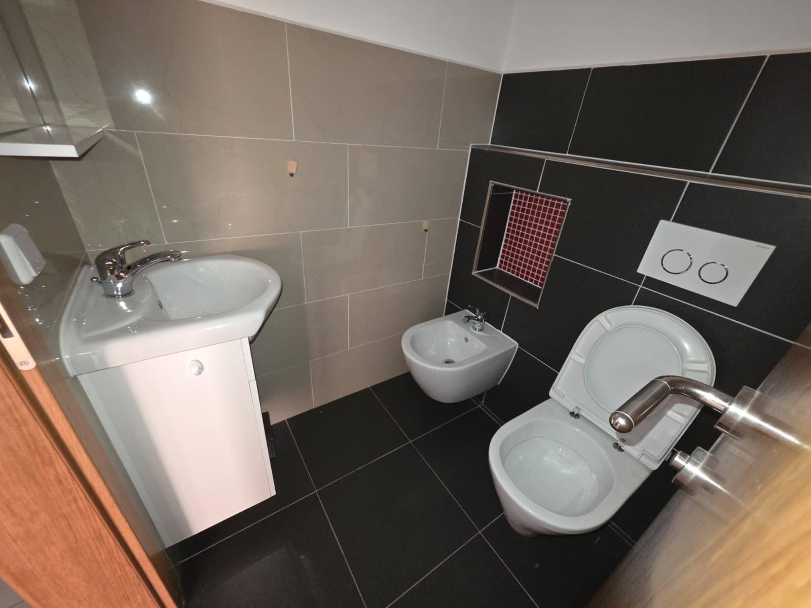 Modernes Gäste-WC mit dunklen Fliesen, Bidet und wandhängendem WC.