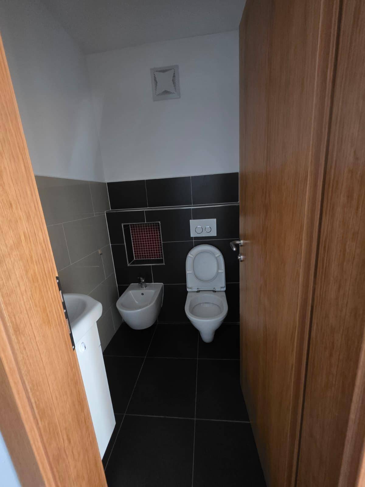 Modernes Gäste-WC mit dunklen Fliesen, Bidet und wandhängendem WC.
