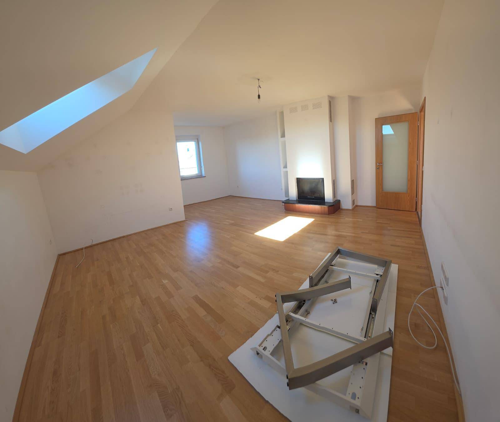 Geräumiger Wohnbereich mit Holzboden, Dachschrägen und einem Kamin als Mittelpunkt.