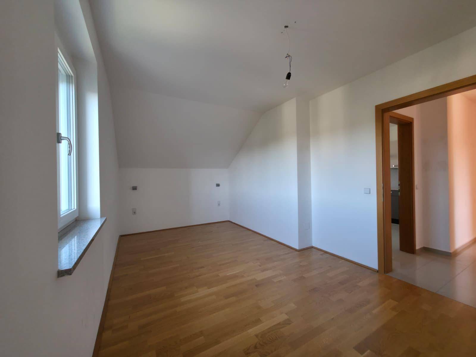 Geräumiges Zimmer mit hellem Holzparkettboden und Zugang zu weiteren Räumen.