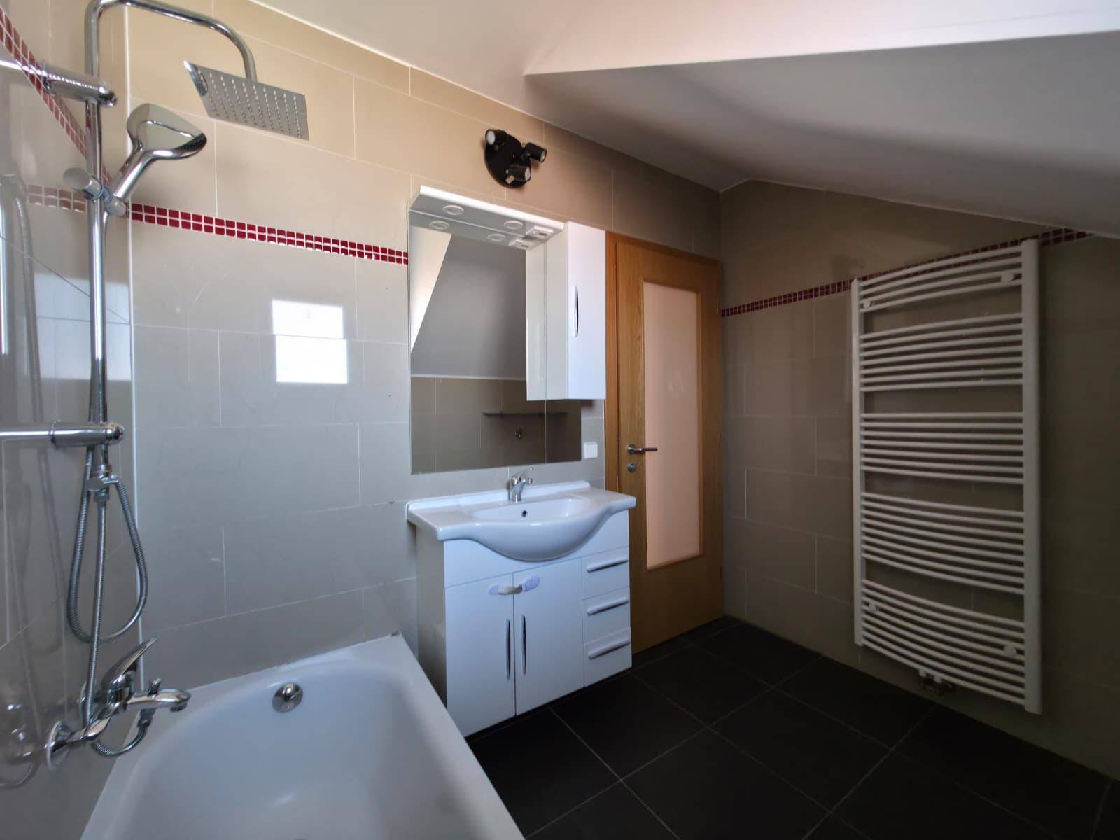 Helles Badezimmer mit Badewanne, Duschkopf, Waschtisch und Handtuchheizkörper unter Dachschräge.