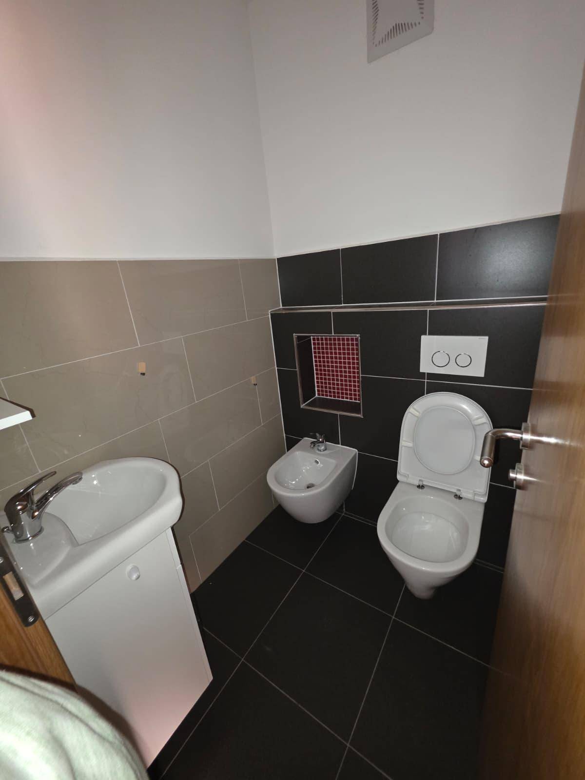 Modernes Gäste-WC mit dunklen Fliesen, Bidet und wandhängendem WC.