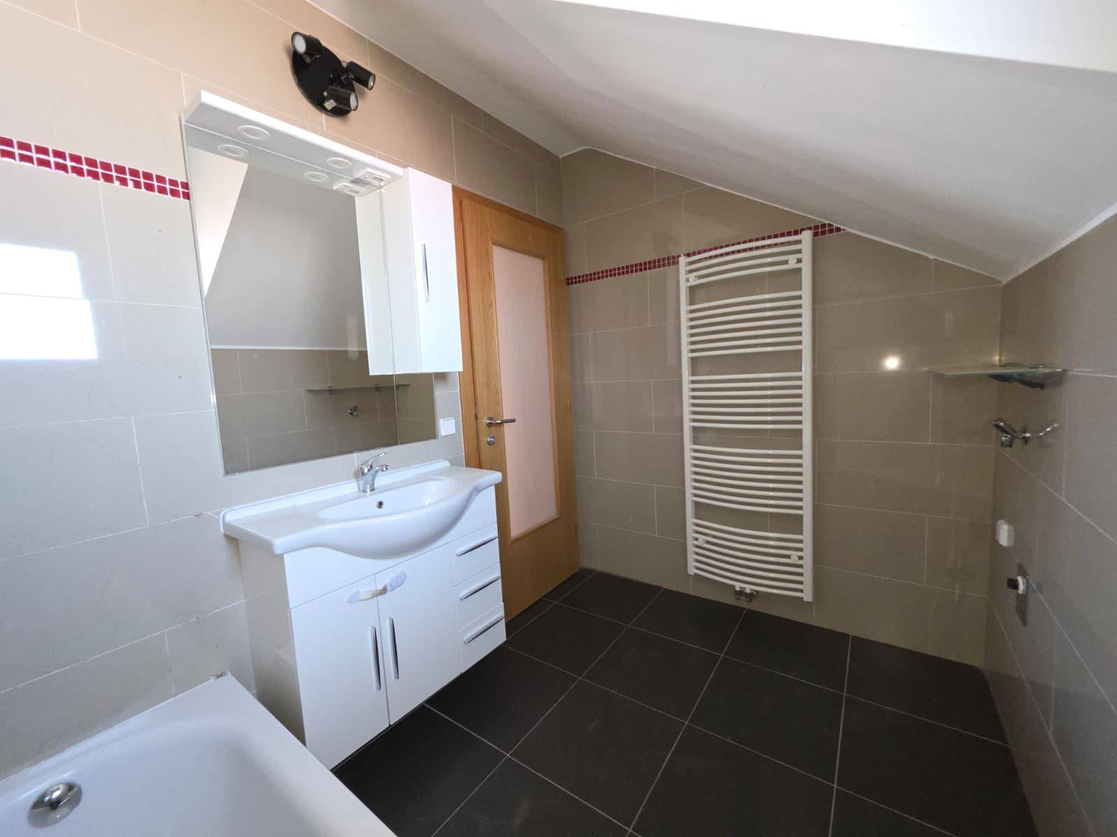 Modernes Badezimmer mit Badewanne, Waschtisch, Spiegelschrank und Handtuchheizkörper unter Dachschräge.