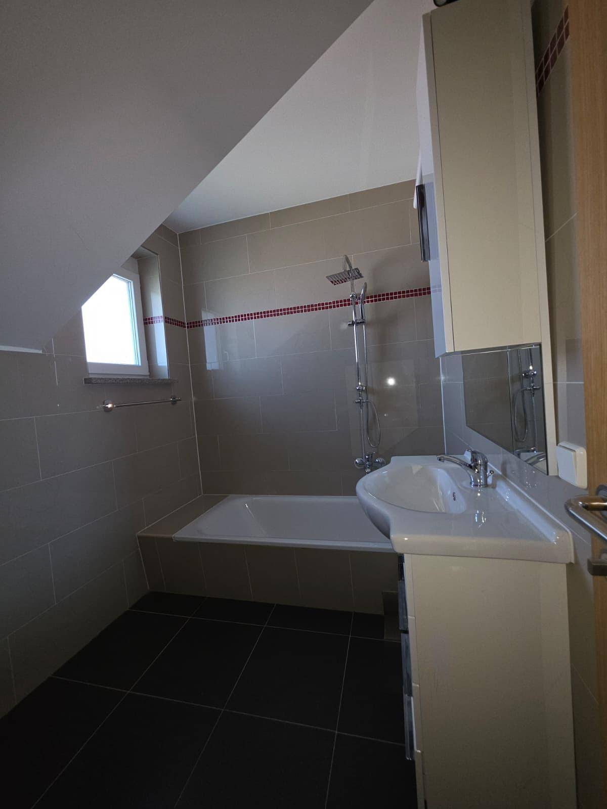 Badezimmer mit Badewanne, Duscharmatur, Waschtisch und Fenster unter der Dachschräge.
