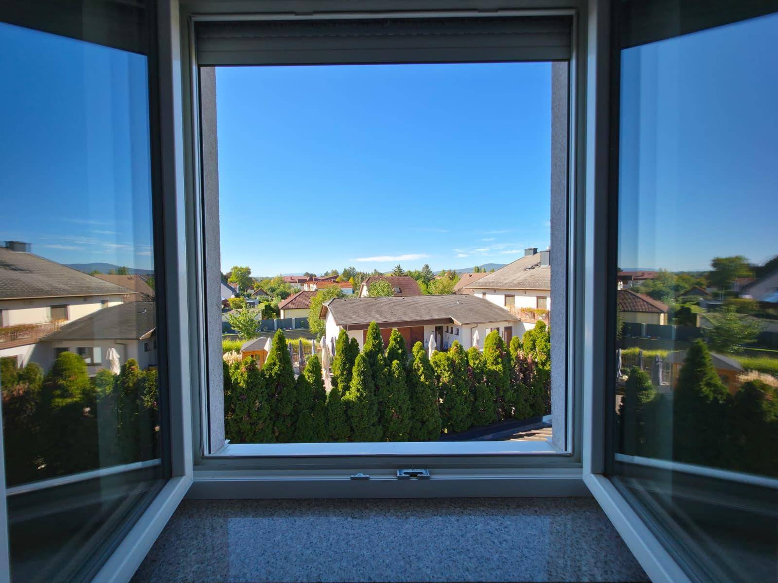Weitblick aus dem Fenster über eine grüne Wohnsiedlung an einem sonnigen Tag.