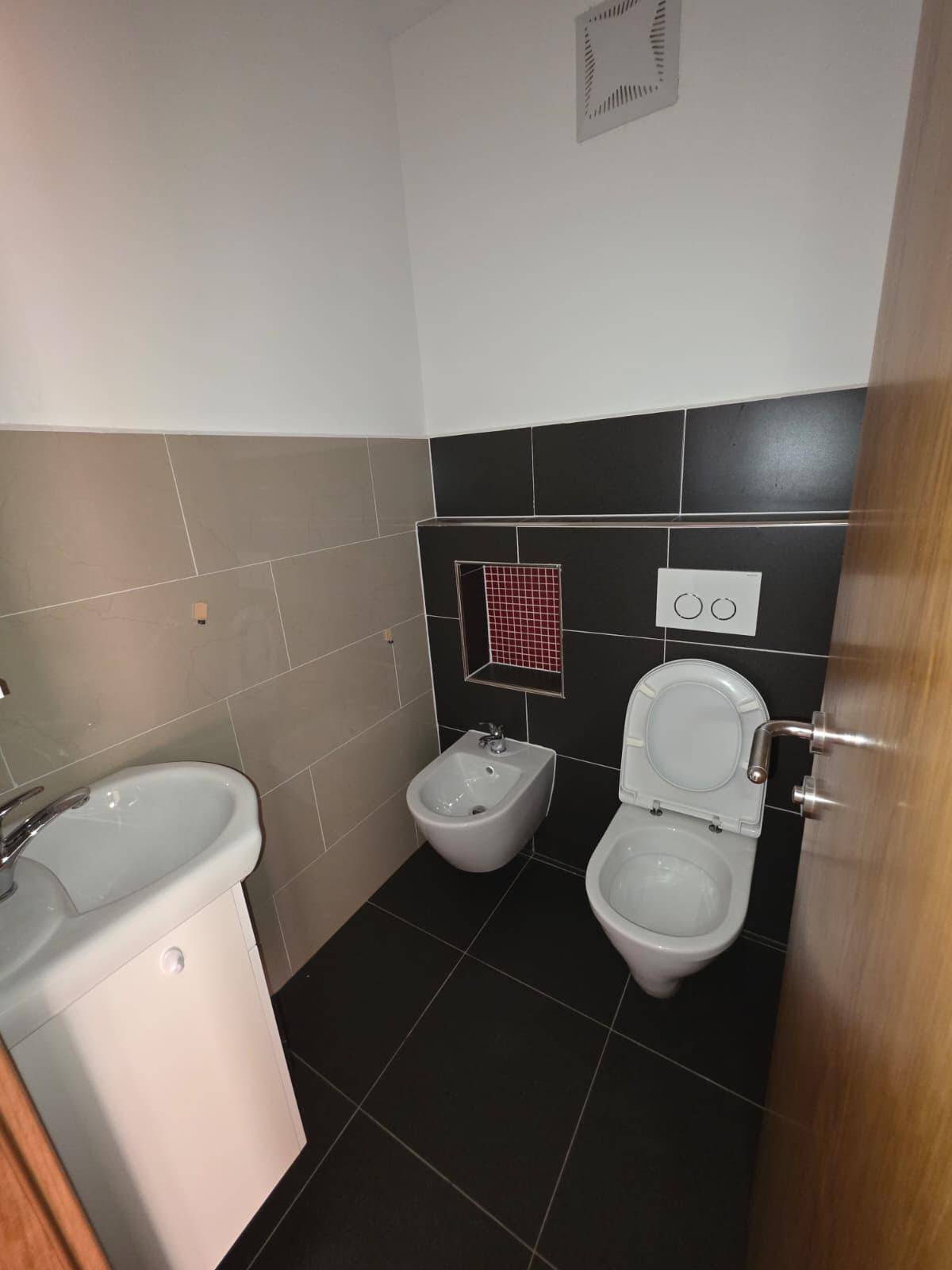 Modernes Gäste-WC mit dunklen Fliesen, Bidet und wandhängendem WC.