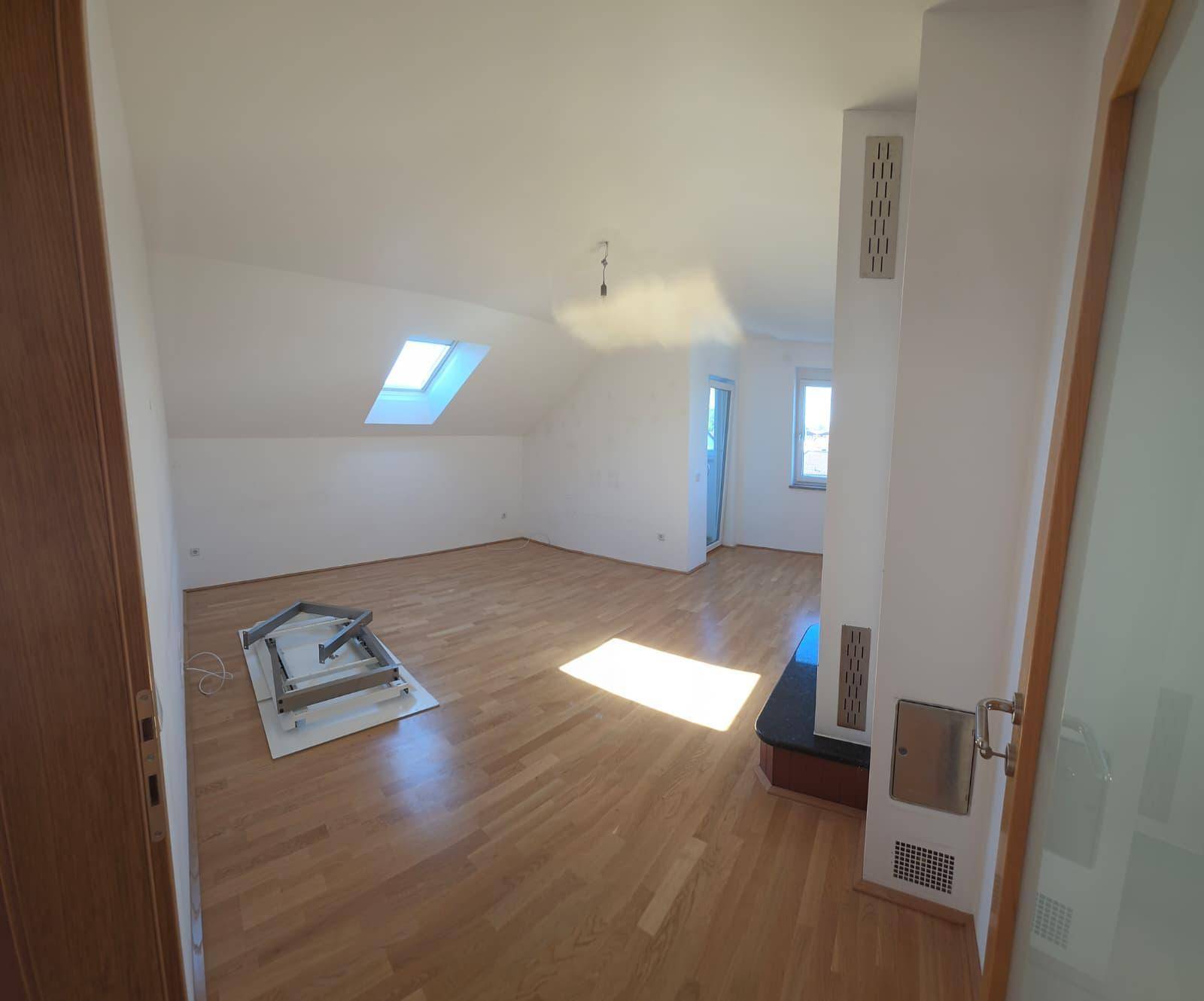 Heller Wohnbereich mit Holzboden, Dachschrägen und einem Dachfenster für natürliches Licht.