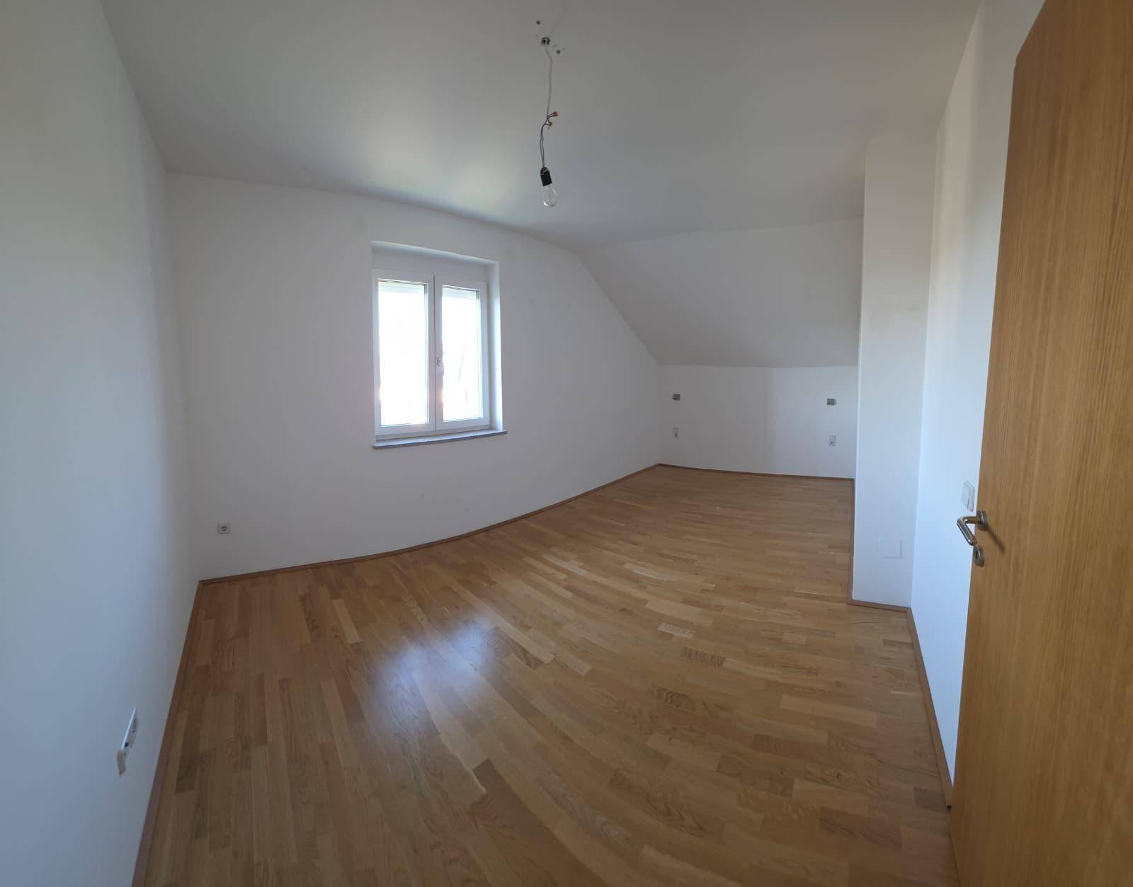 Helles Zimmer mit Holzparkettboden, weißen Wänden und Fenster unter der Dachschräge.