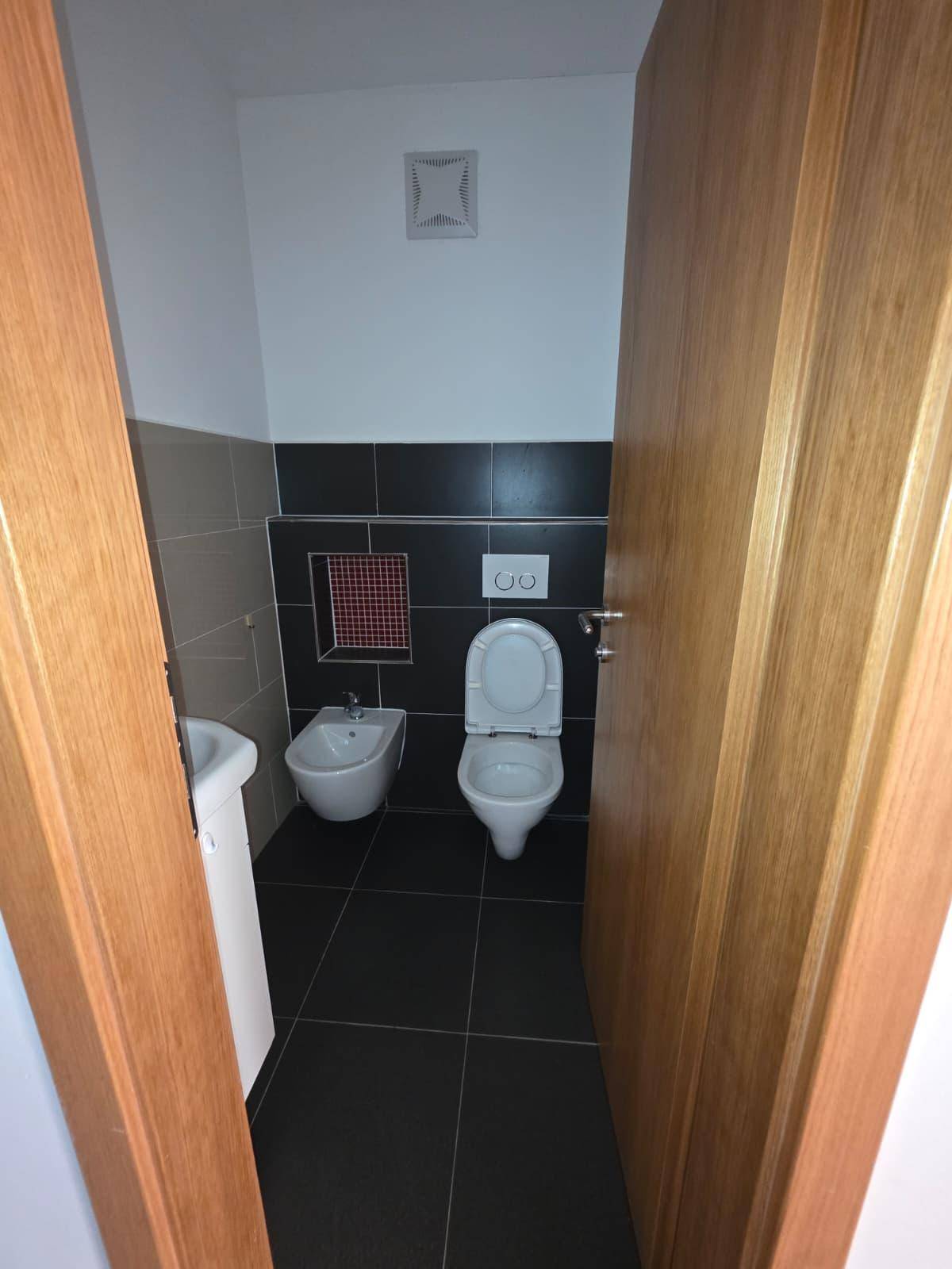 Modernes Gäste-WC mit dunklen Fliesen, Bidet und wandhängendem WC.
