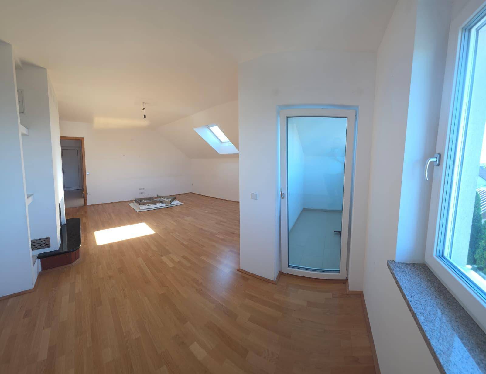 Heller Wohnbereich mit Holzboden, Dachschrägen und Zugang zu einem kleinen Balkon oder Loggia.