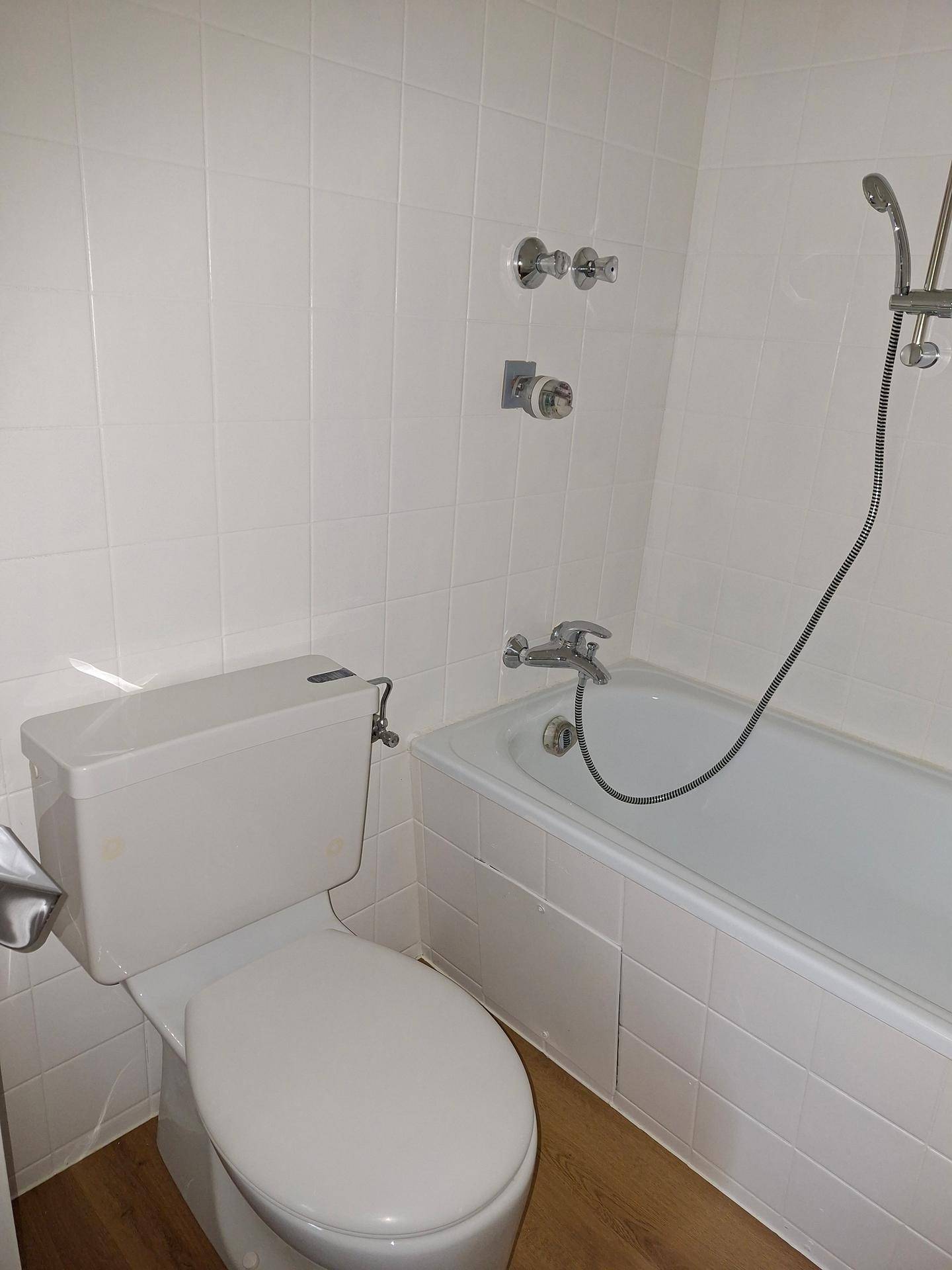 Nahaufnahme der Badewanne und Toilette in einem weiß gefliesten Badezimmer.