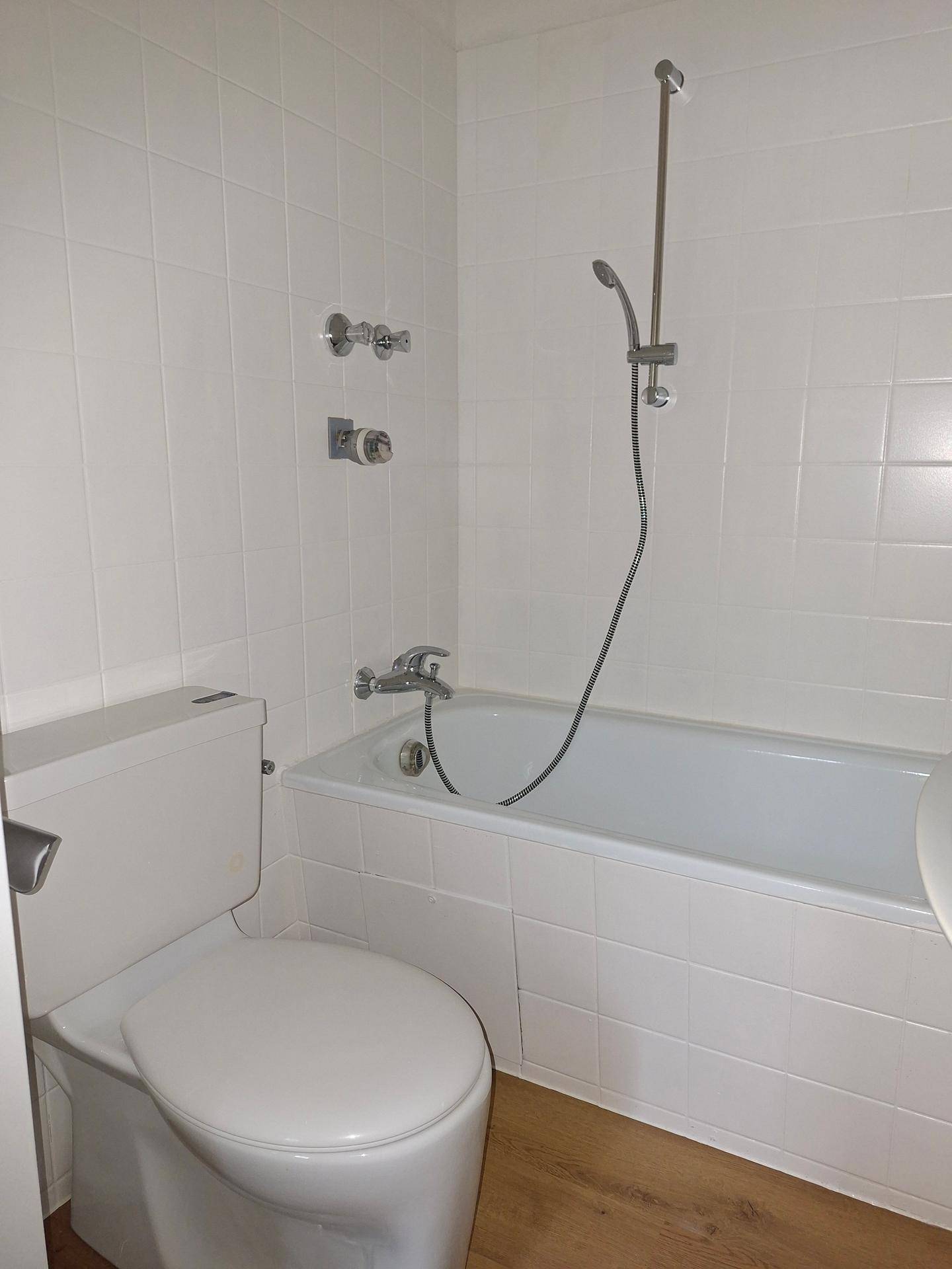 Nahaufnahme der Badewanne und Toilette in einem weiß gefliesten Badezimmer.