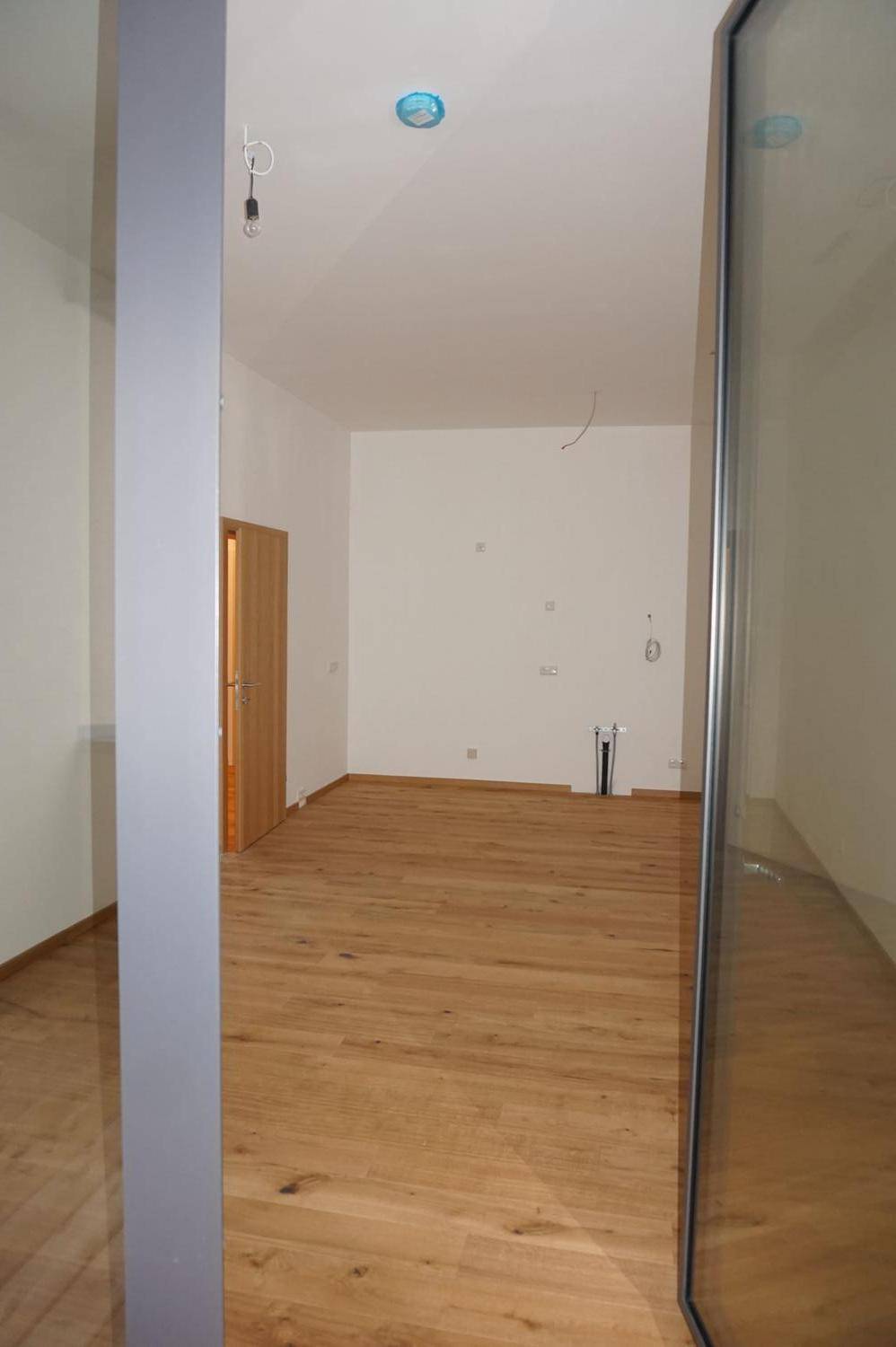 Geräumiger Raum mit Holzboden und vorbereiteten Anschlüssen für die Kücheninstallation, von der Seite gesehen.