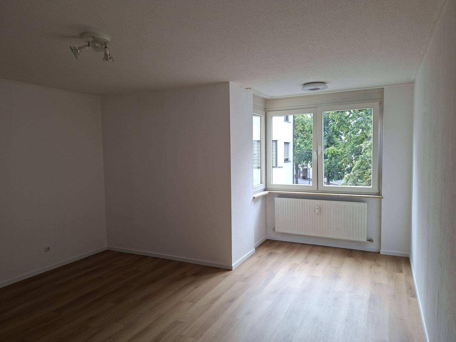 Geräumiger Wohnbereich mit hellem Laminatboden und Ausblick ins Grüne durch die Fenster.