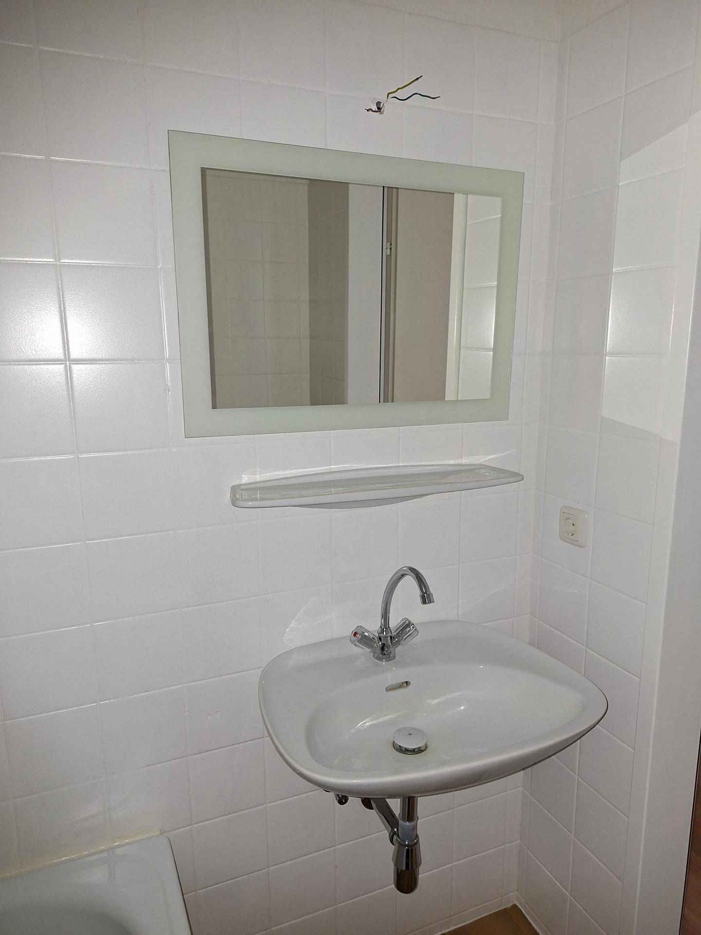 Waschbecken mit Spiegel in einem hell gefliesten Badezimmer, funktional und sauber.