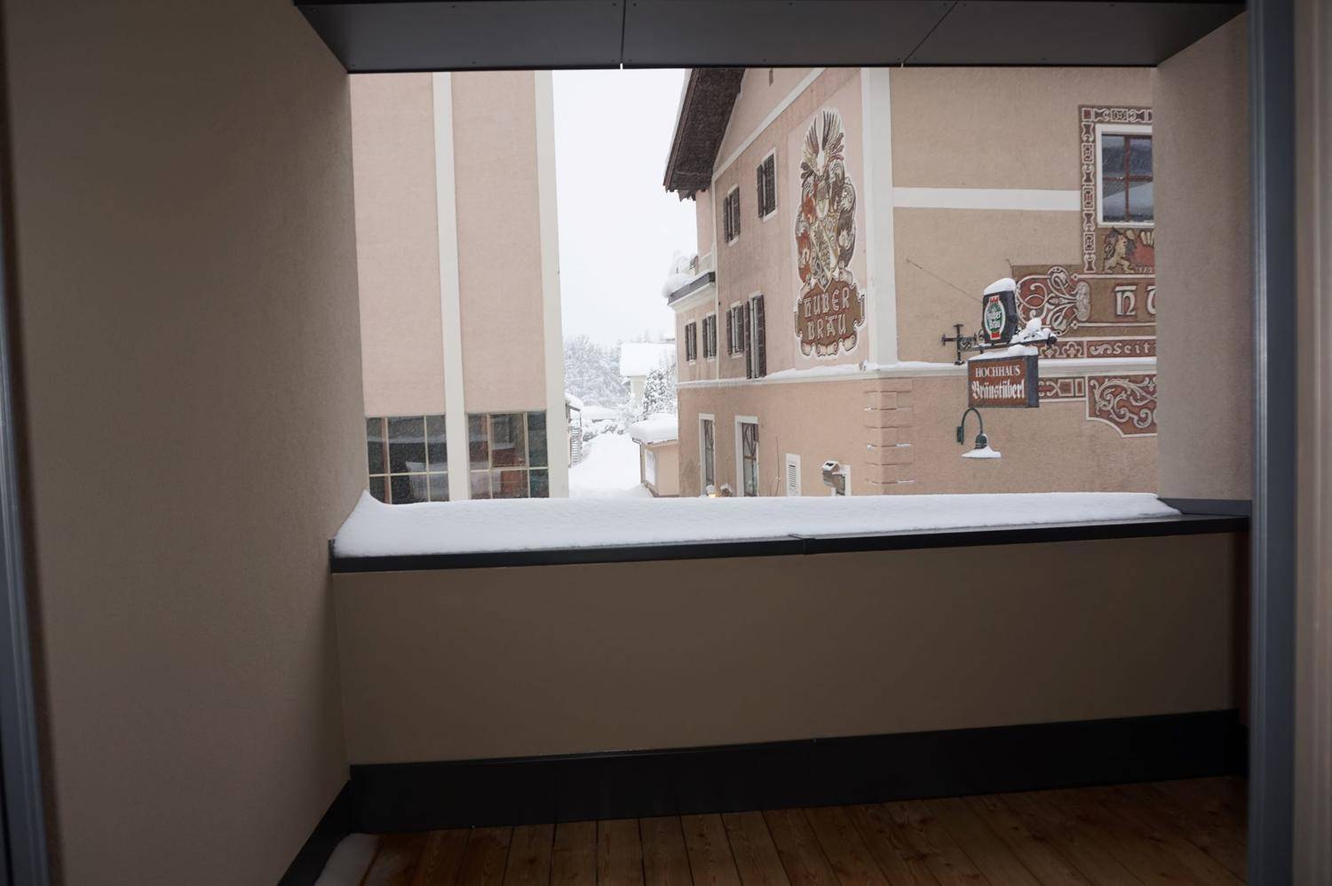 Kleiner Balkon mit Holzboden und Blick auf eine verschneite Straße mit traditionellen Gebäuden.