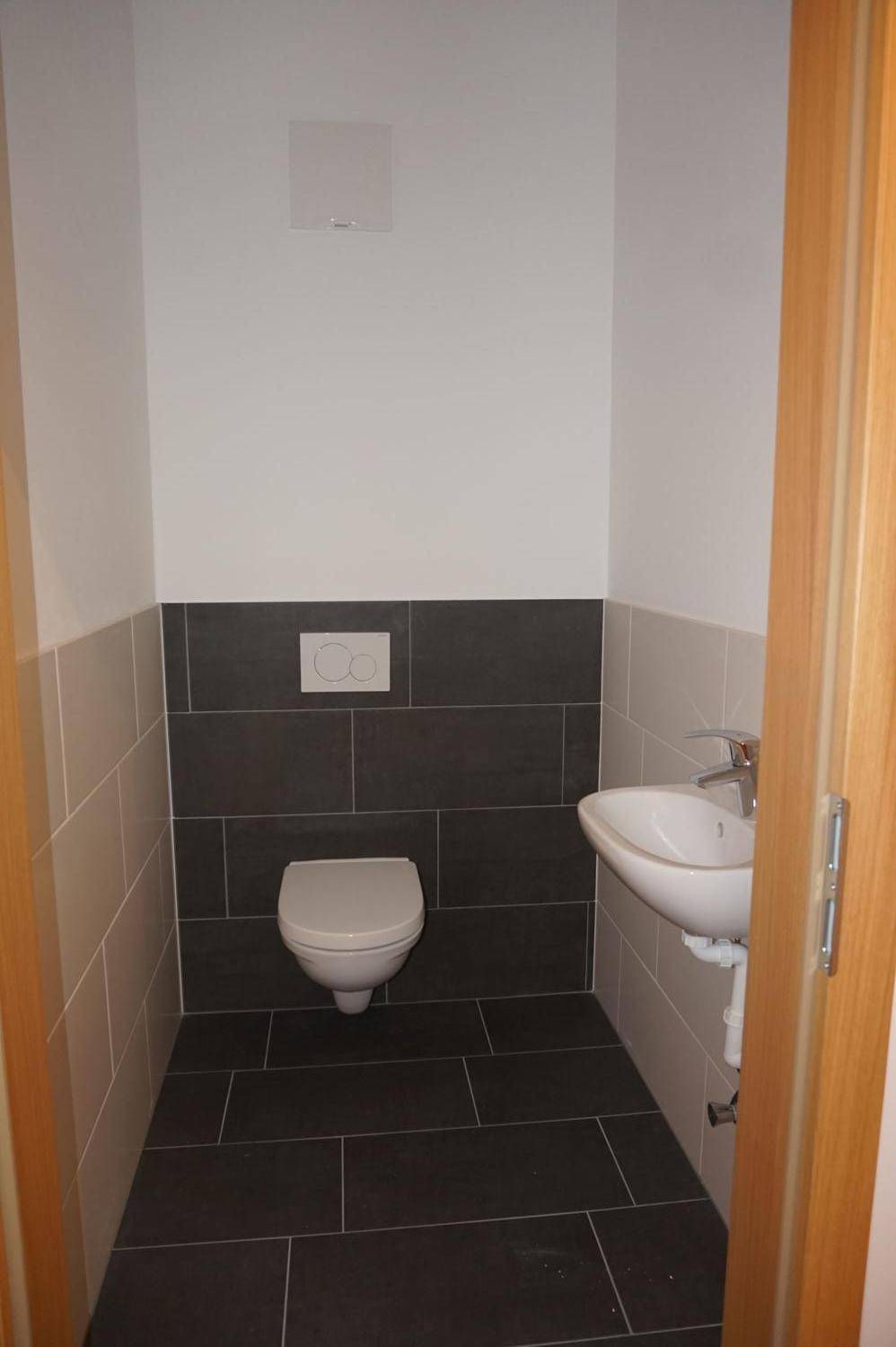 Modernes Gäste-WC mit wandhängender Toilette, kleinem Waschbecken und zweifarbigen Fliesen.