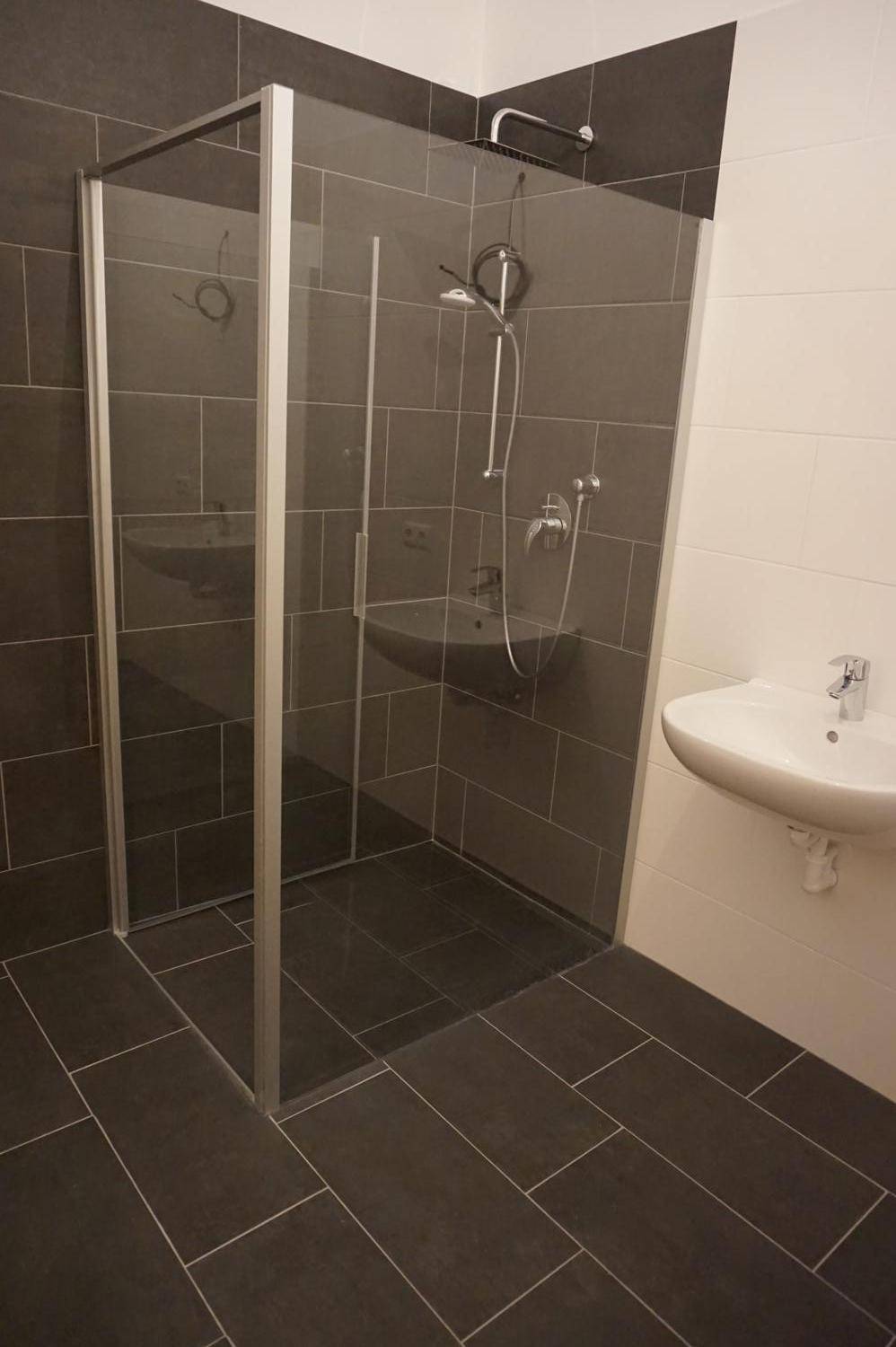 Geräumige Duschkabine mit Glasabtrennung und modernen dunklen Fliesen im Badezimmerbereich.