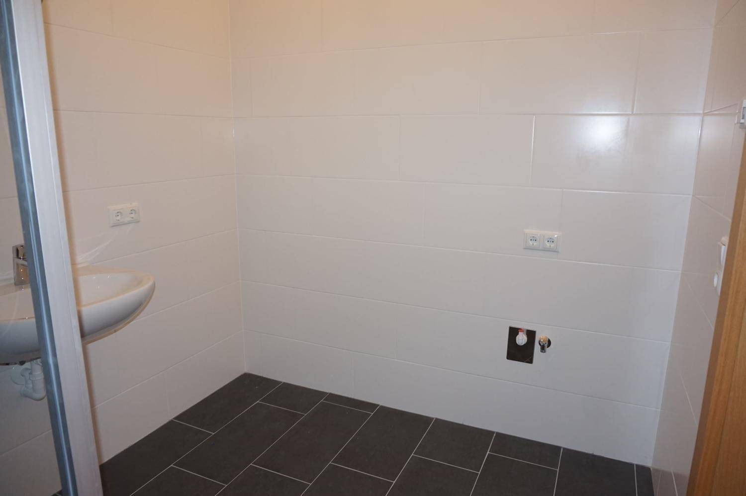 Teil des Badezimmers mit Waschbecken und vorbereiteten Anschlüssen für weitere Installationen an der Wand.