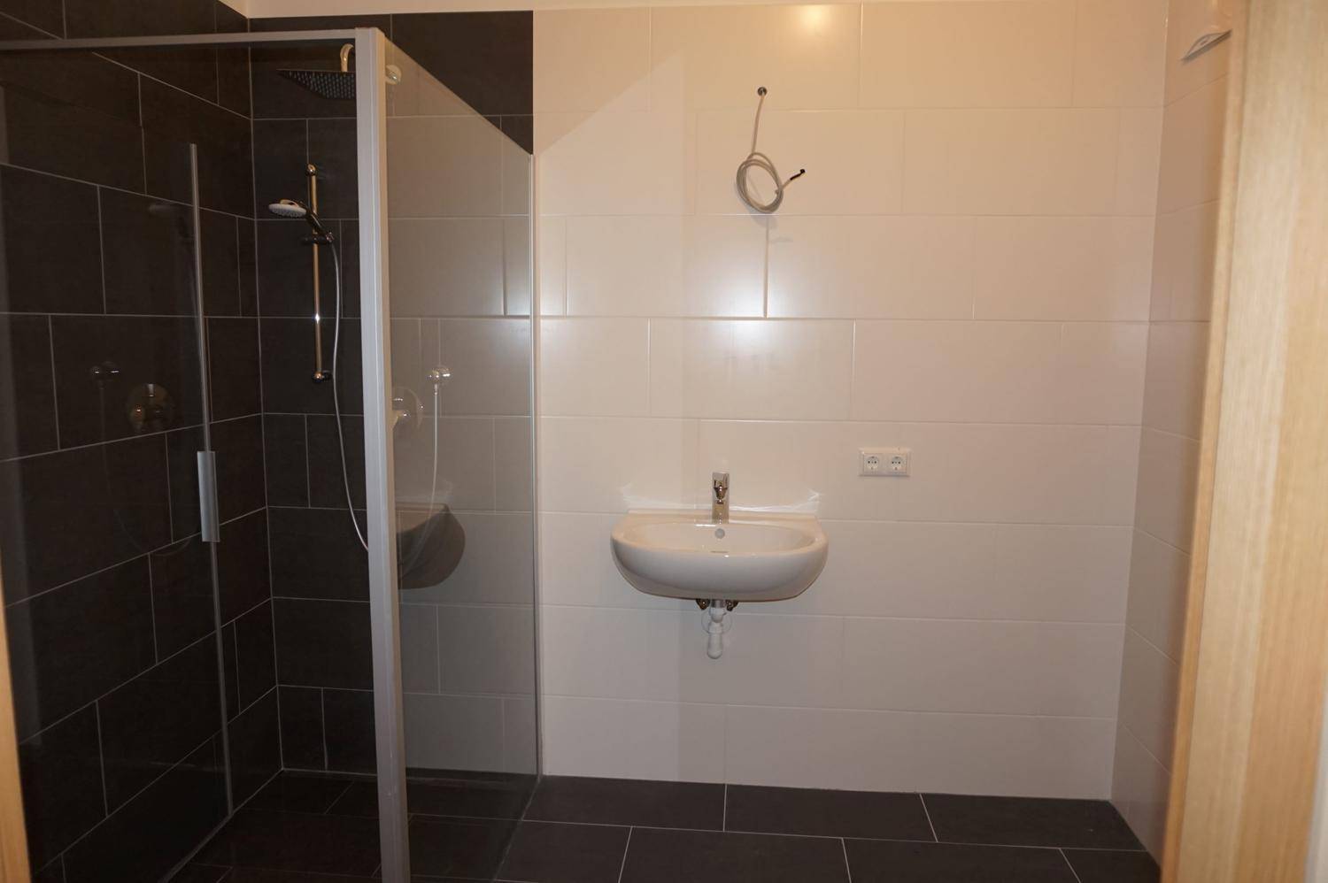 Modernes Badezimmer mit ebenerdiger Dusche, Waschbecken und dunklen Fliesen an Wänden und Boden.