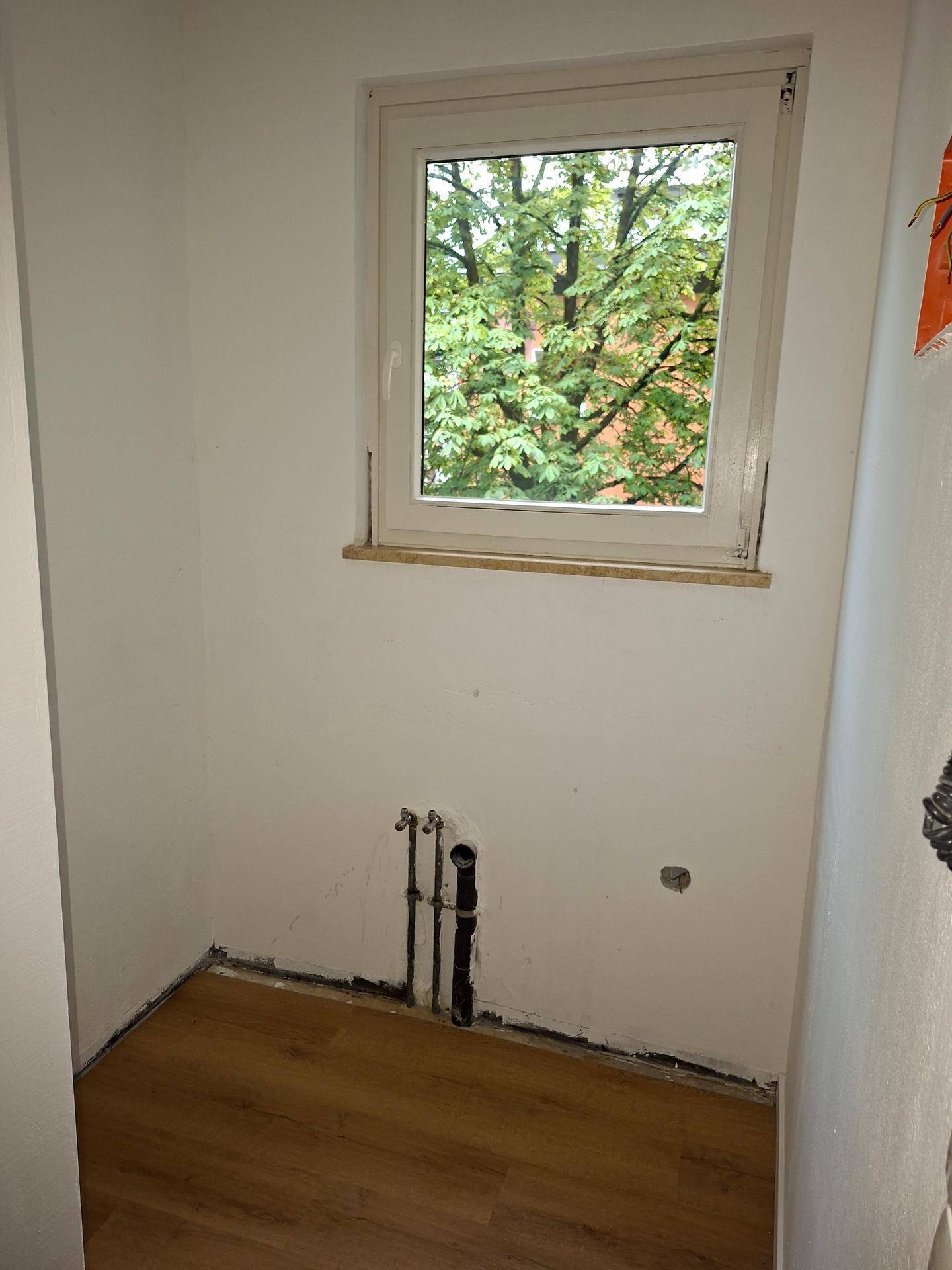 Kleiner Raum mit sichtbaren Wasseranschlüssen und einem Fenster, ideal als Hauswirtschaftsraum.