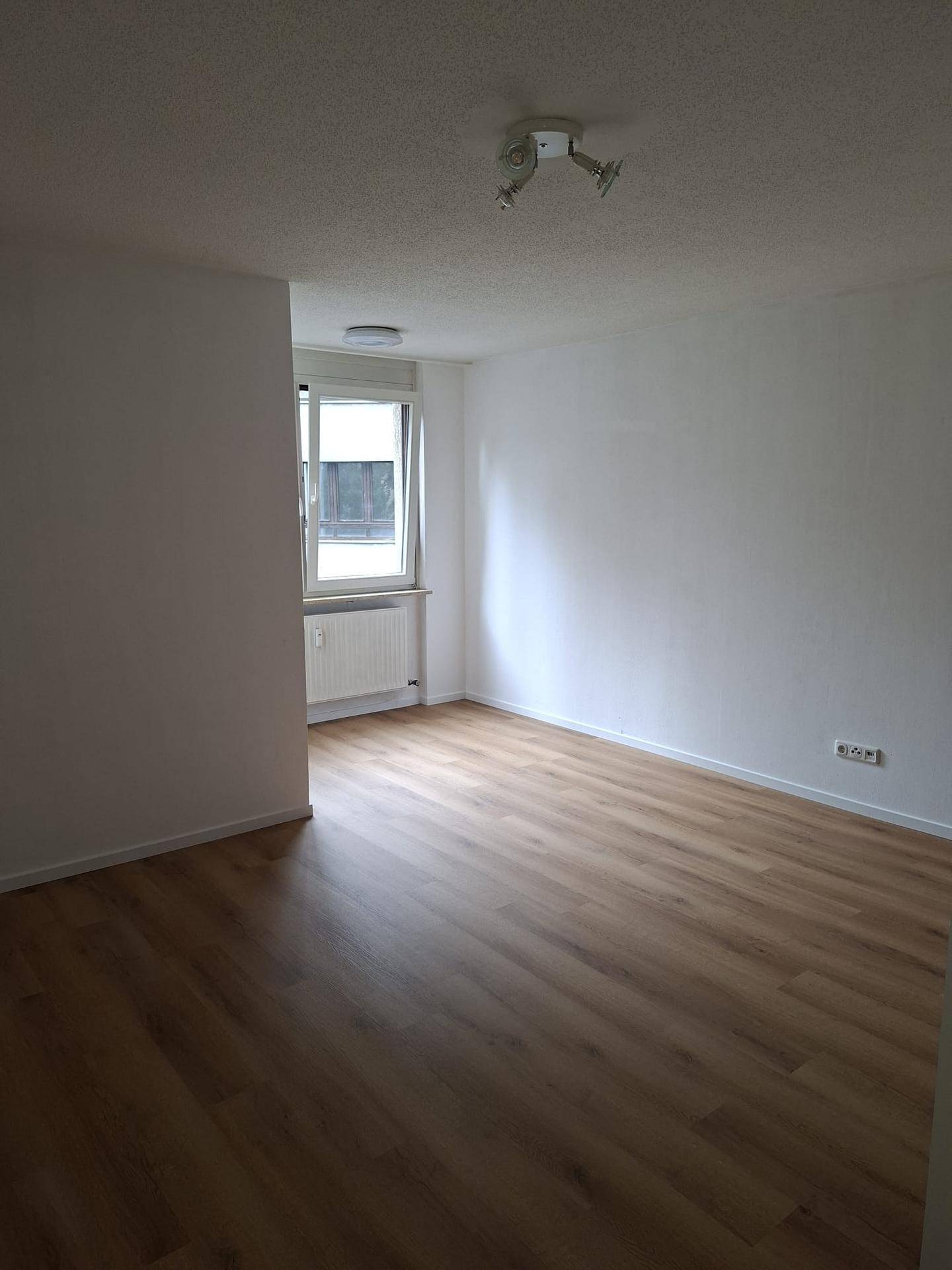Heller Wohnraum mit Laminatboden und einem Fenster, das Tageslicht in den Raum lässt.